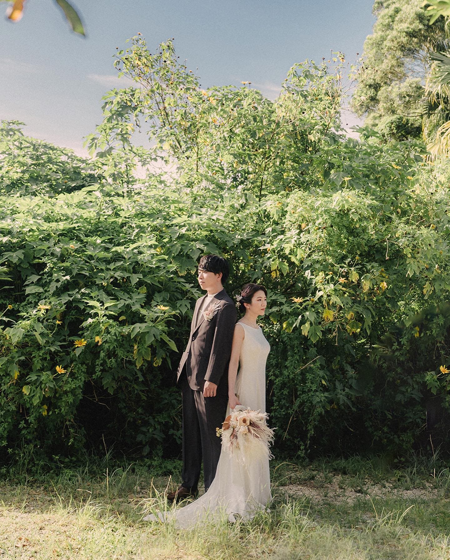 A couple posing with a bouquet before dense green foliage in Okinawa