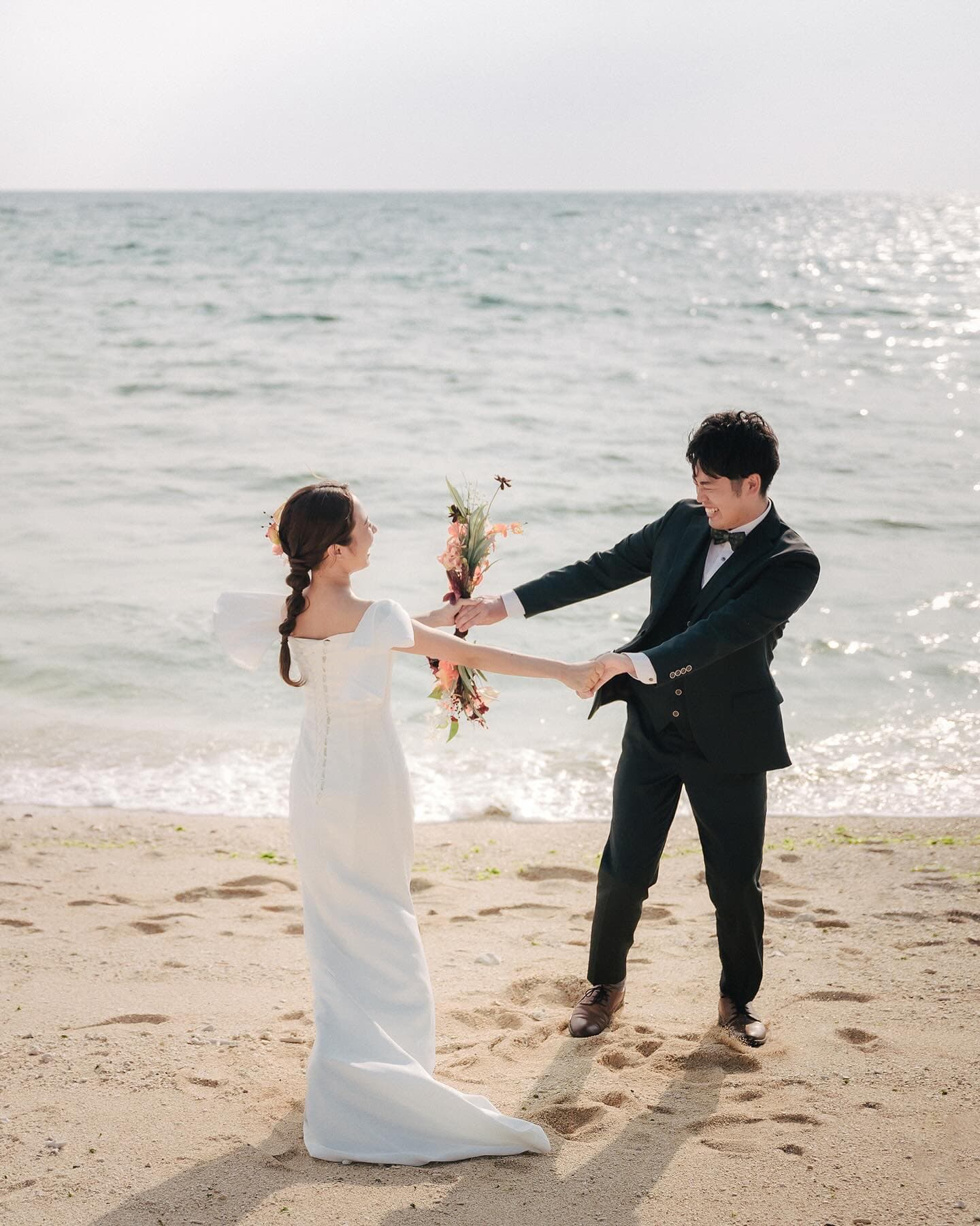 Couple holding both hands at the water's edge with a bouquet on an Okinawa beach