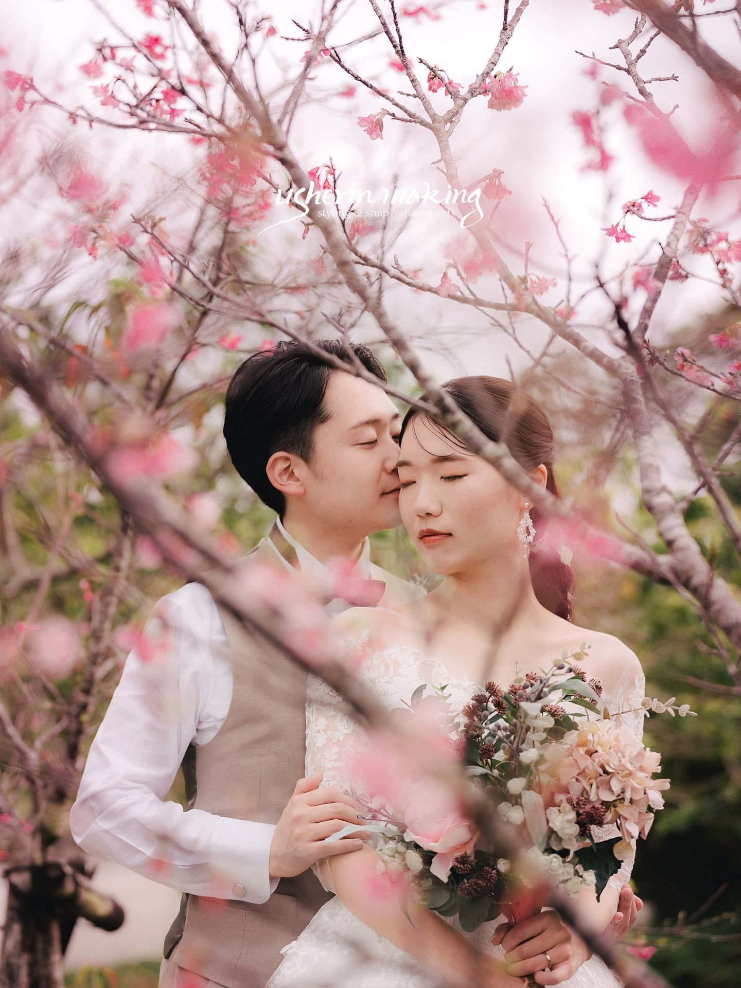 桜の枝越しに寄り添う新郎新婦、ブーケを抱く花嫁、沖縄の冬の前撮り