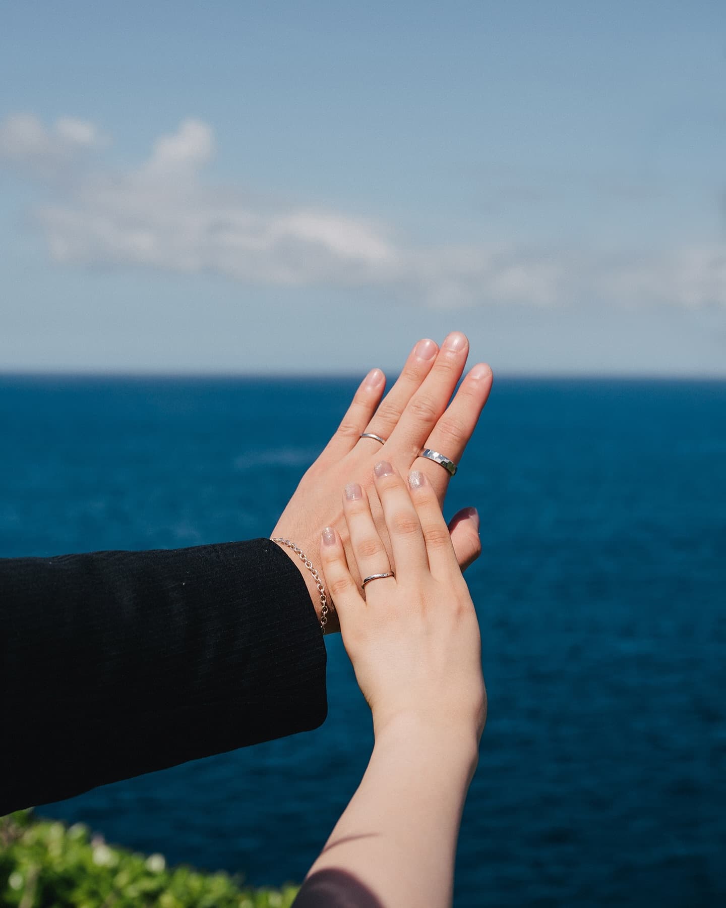 紺碧の海を背景に結婚指輪をつけた二人の手を合わせるクローズアップ、沖縄