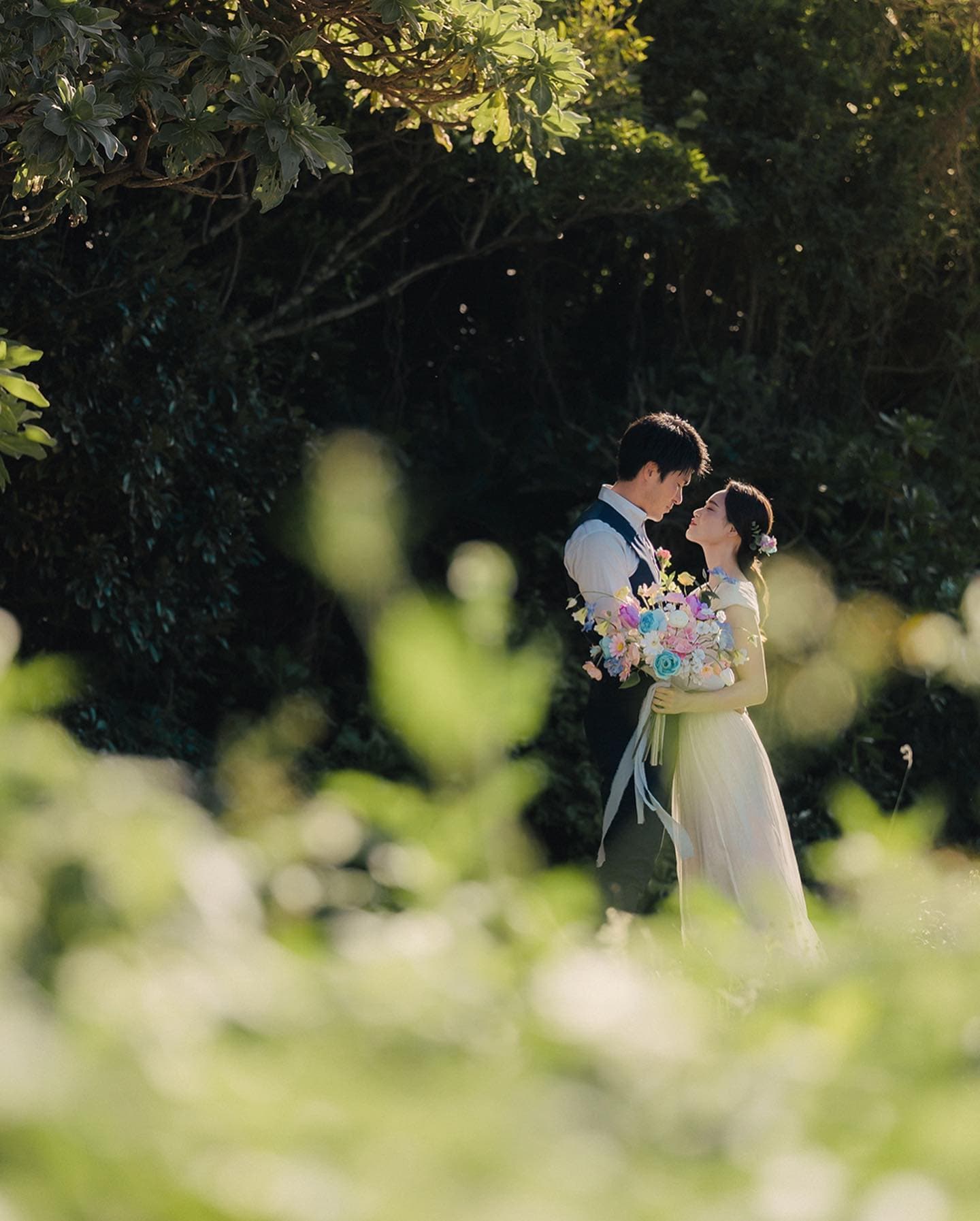 Couple gazing at each other with a colorful bouquet amid sunlit Okinawa greenery