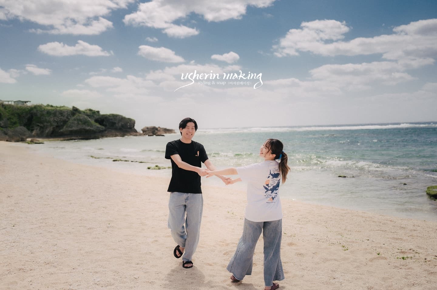 A couple joins both hands, laughing on the sunny shoreline in Okinawa