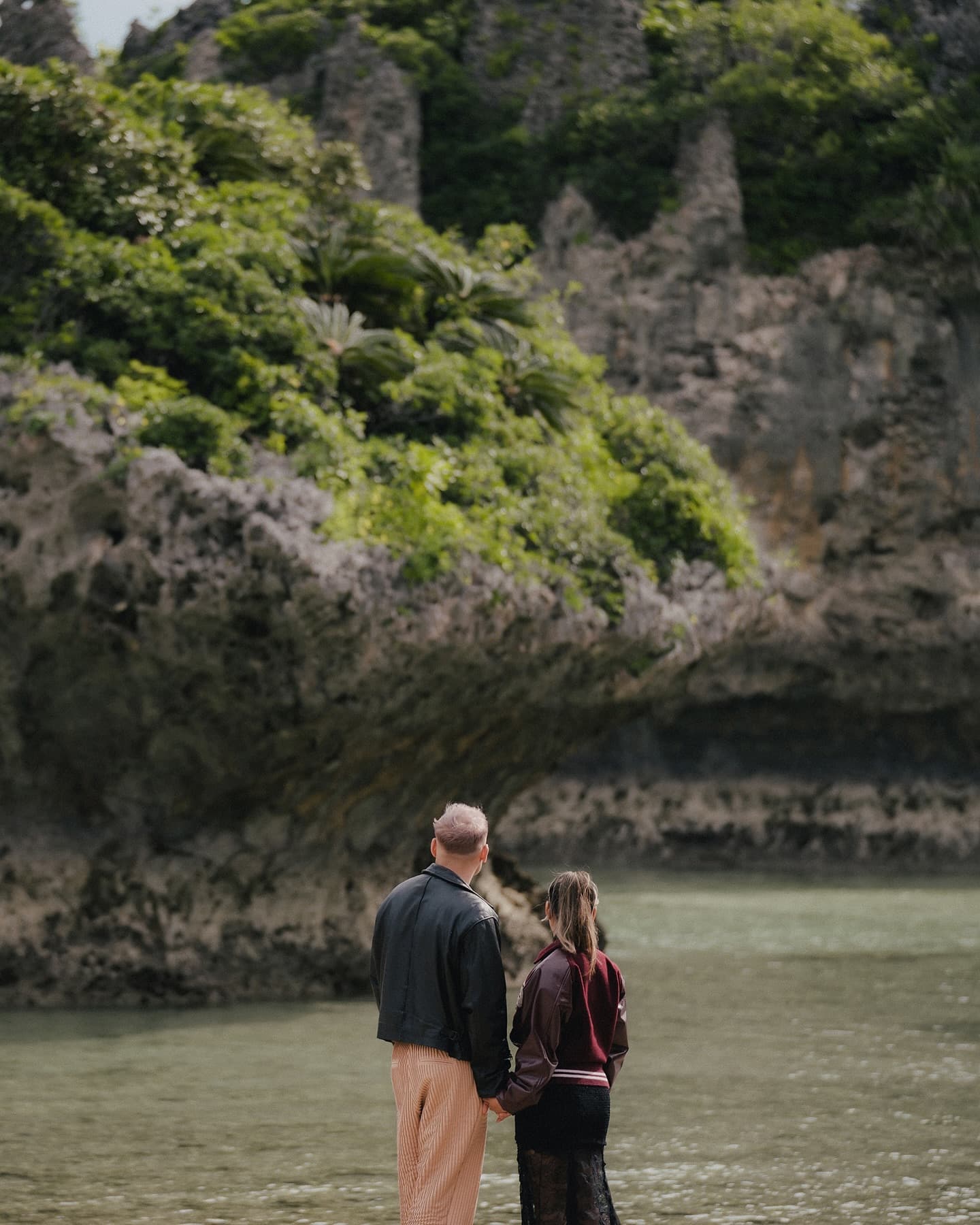 Back view of a couple holding hands by a jungle-framed lagoon, Okinawa