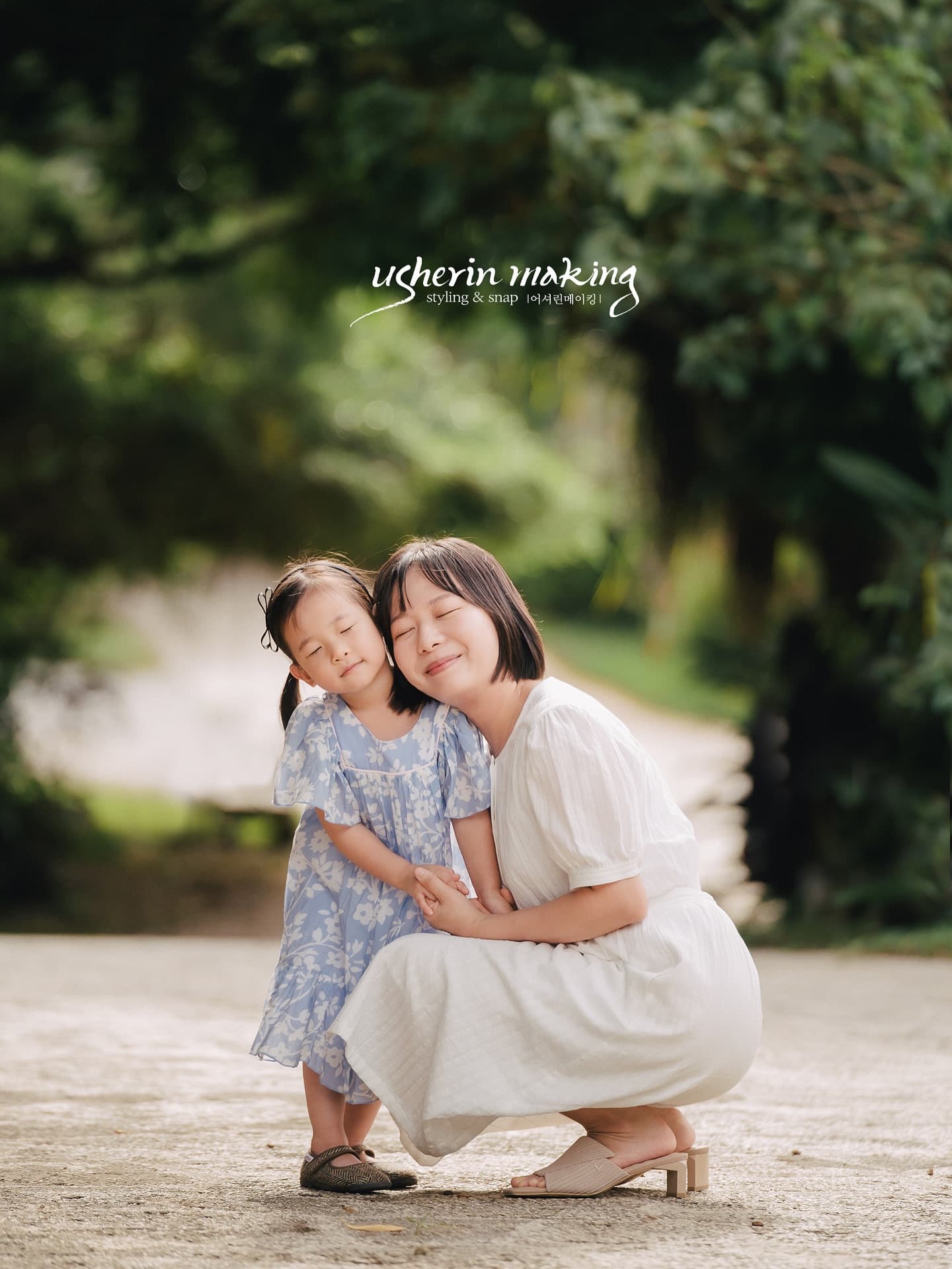 A mother hugs her daughter cheek to cheek on a leafy Okinawa path