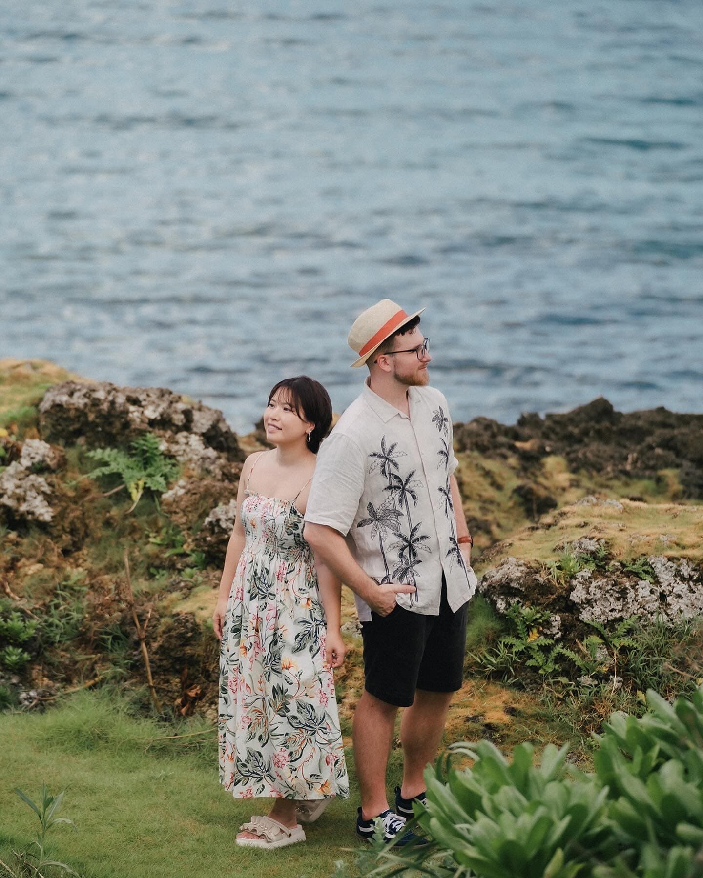 Couple standing on rocky coastal greenery gazing at Okinawa's blue sea