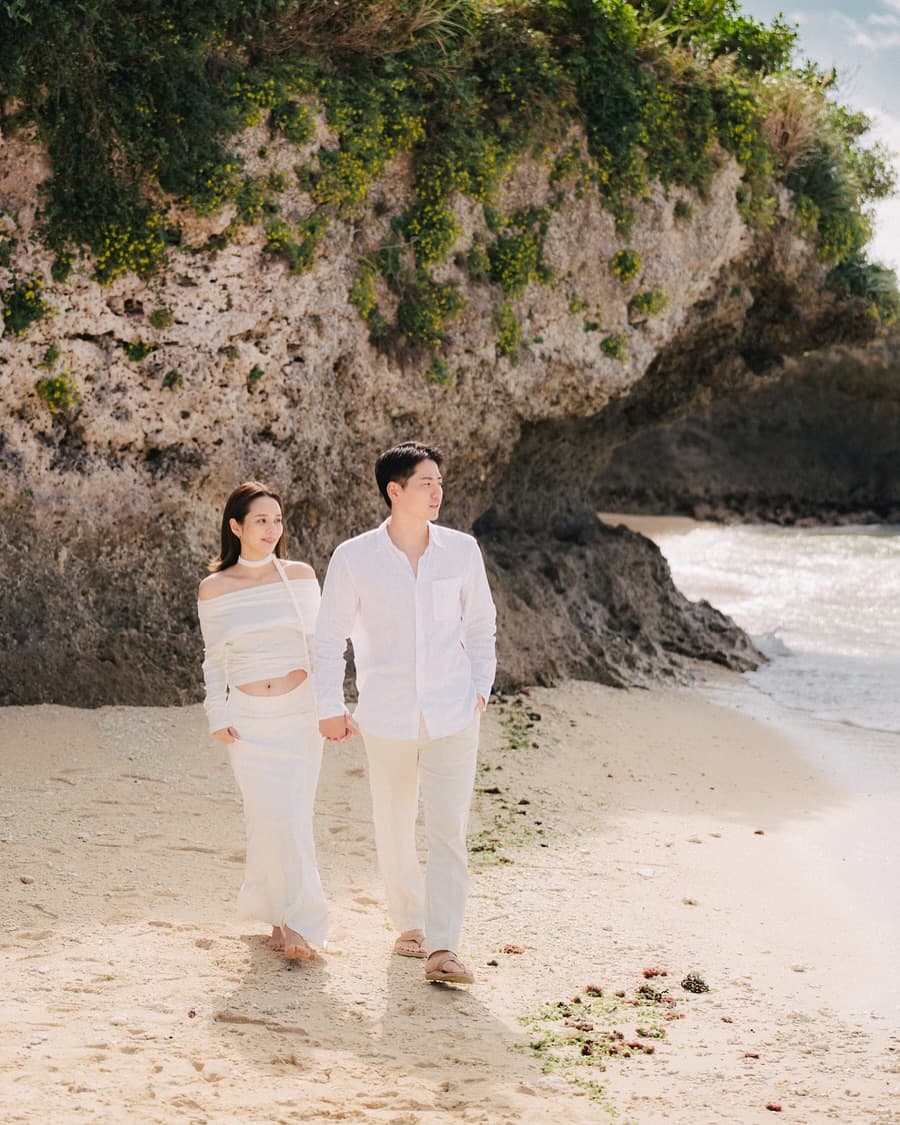 Couple strolling along the shore beneath a green sea cliff in Okinawa