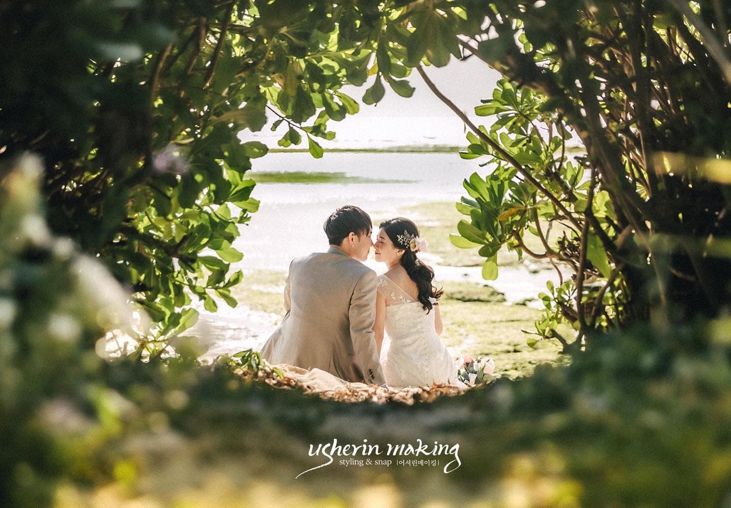 Framed by an arch of green leaves, a couple sits together facing the tidal shore in Okinawa.
