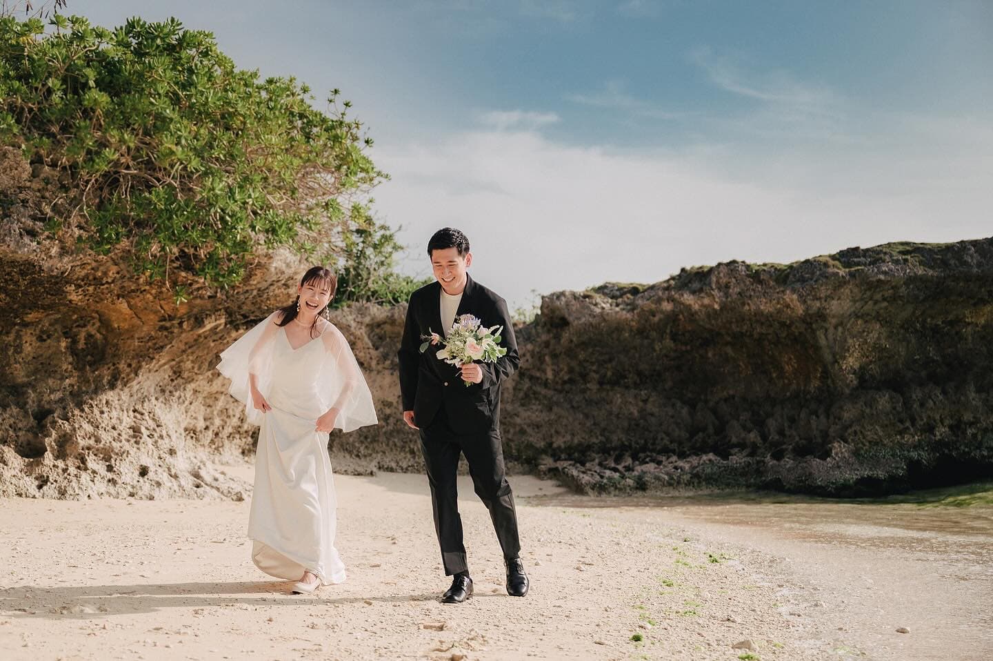 Bride and groom strolling an Okinawa beach lined with rocky cliffs