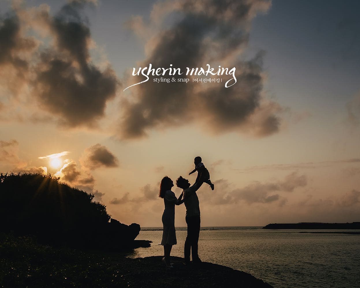 Silhouette of parents lifting their baby high against a sunset sea in Okinawa.