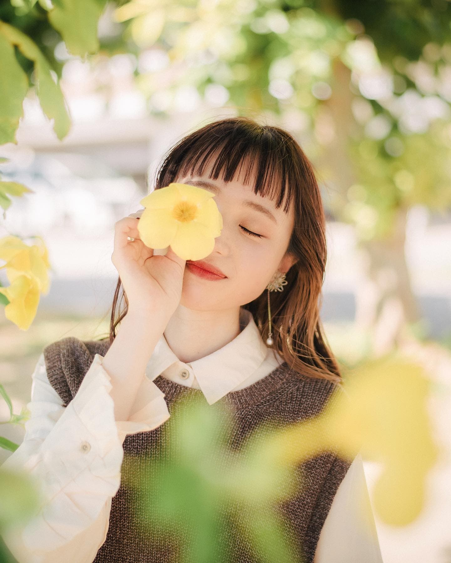 黄色い花を目元にかざして微笑む女性の沖縄ポートレート