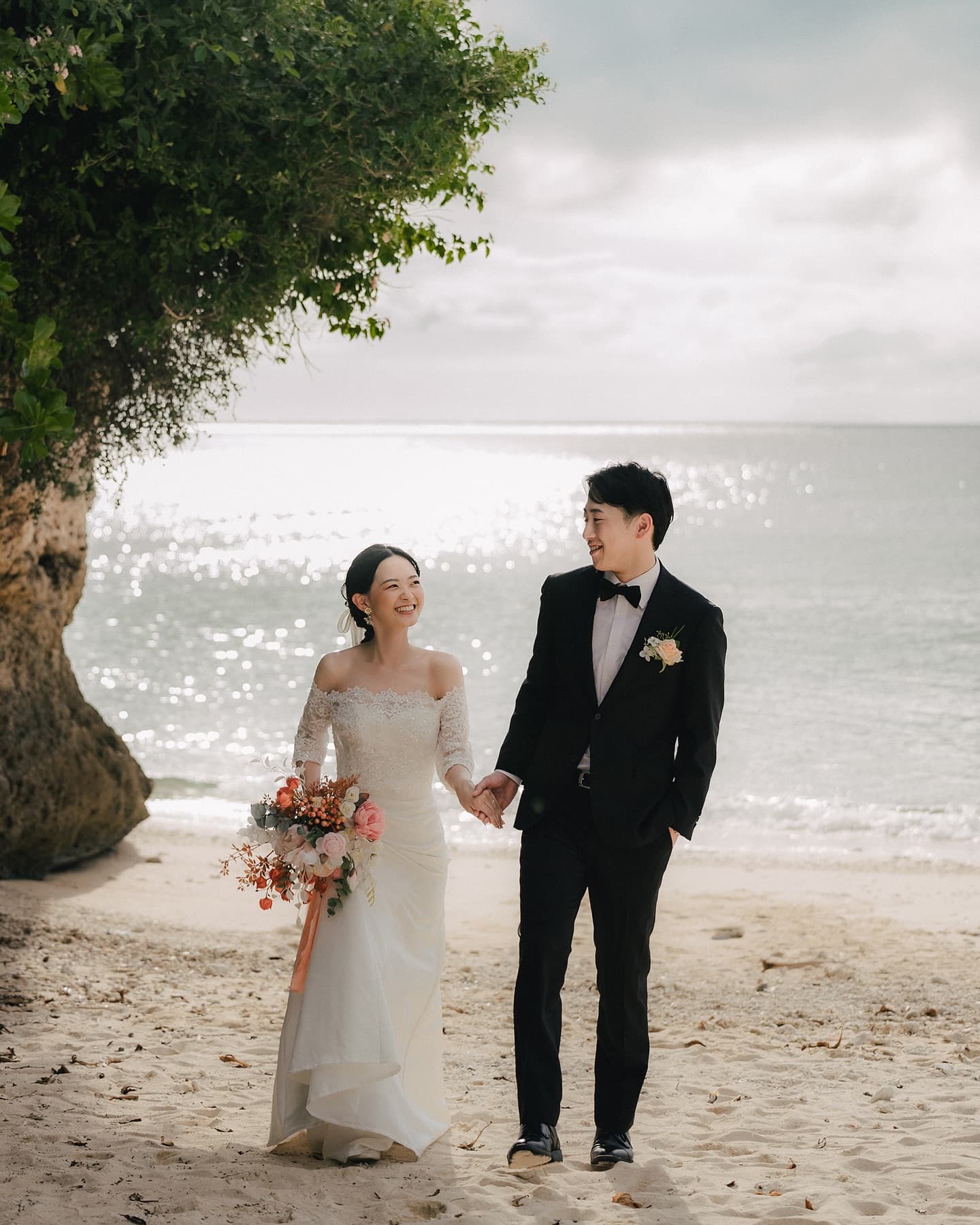 Bride and groom walking hand in hand on a softly backlit Okinawa beach