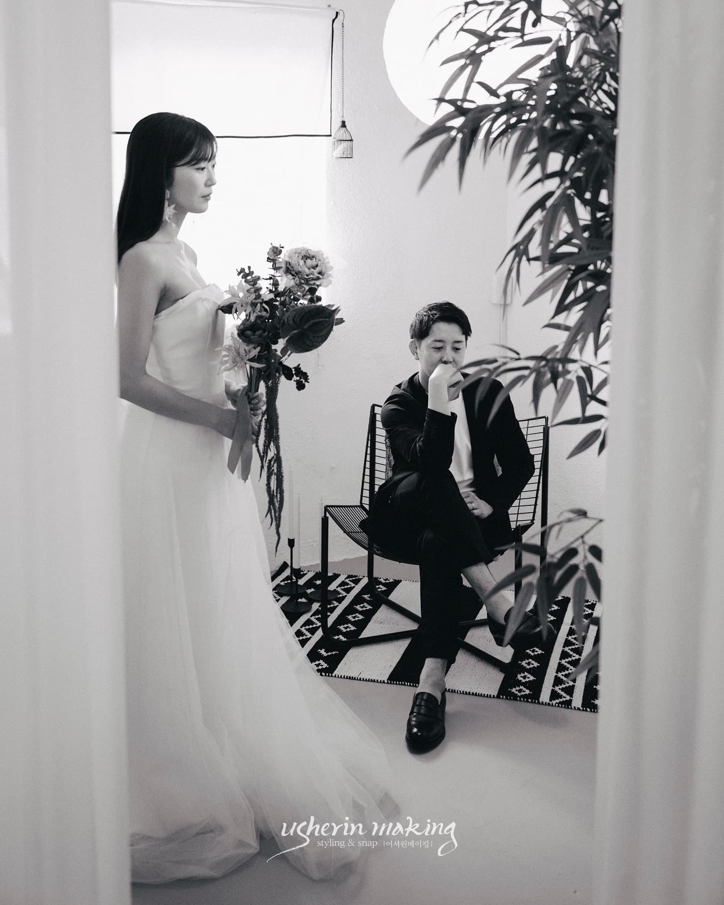 Black-and-white studio portrait of the bride with a bouquet and the groom seated behind