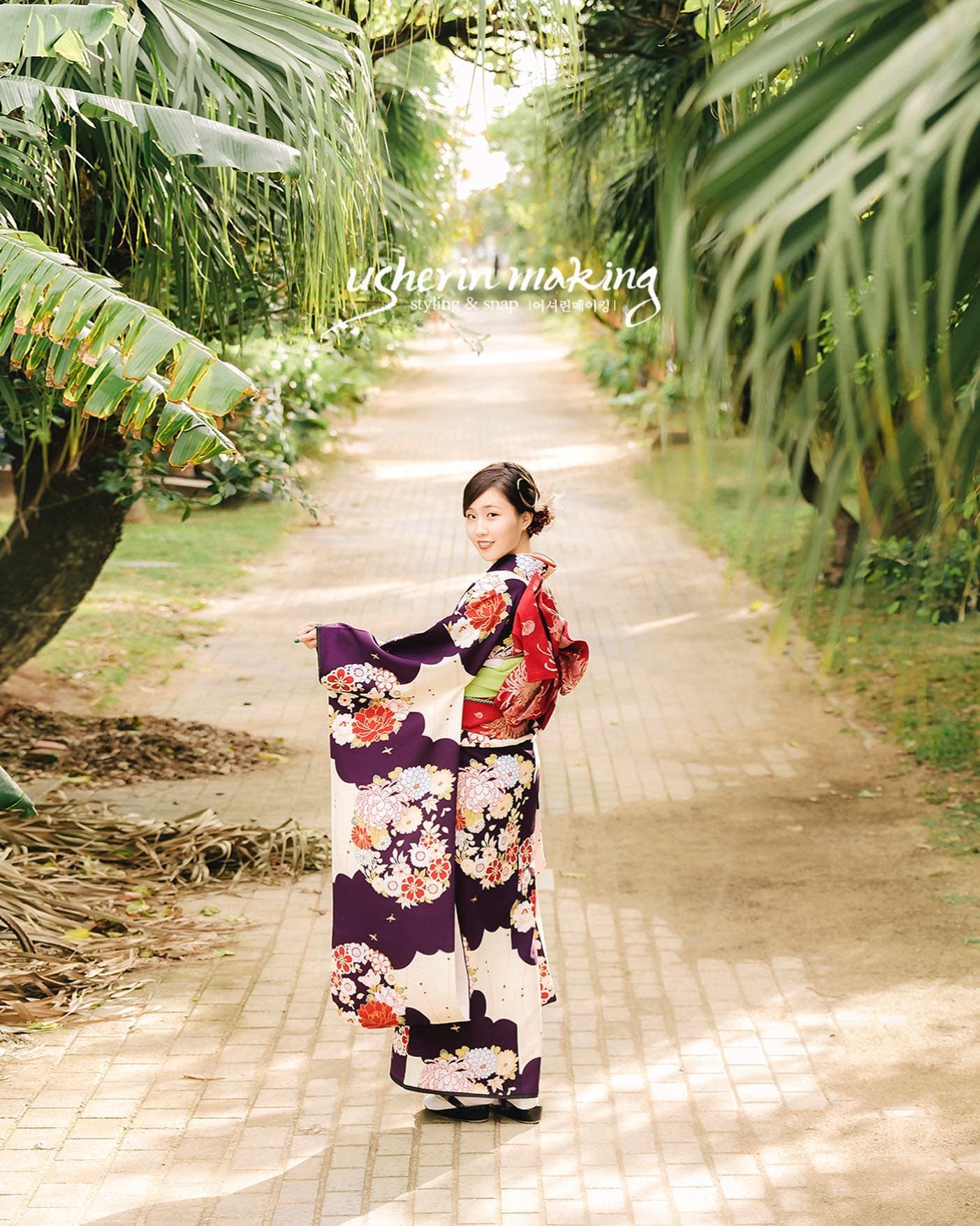 ヤシ並木の道で振り返る振袖姿の女性。沖縄での成人式記念写真。