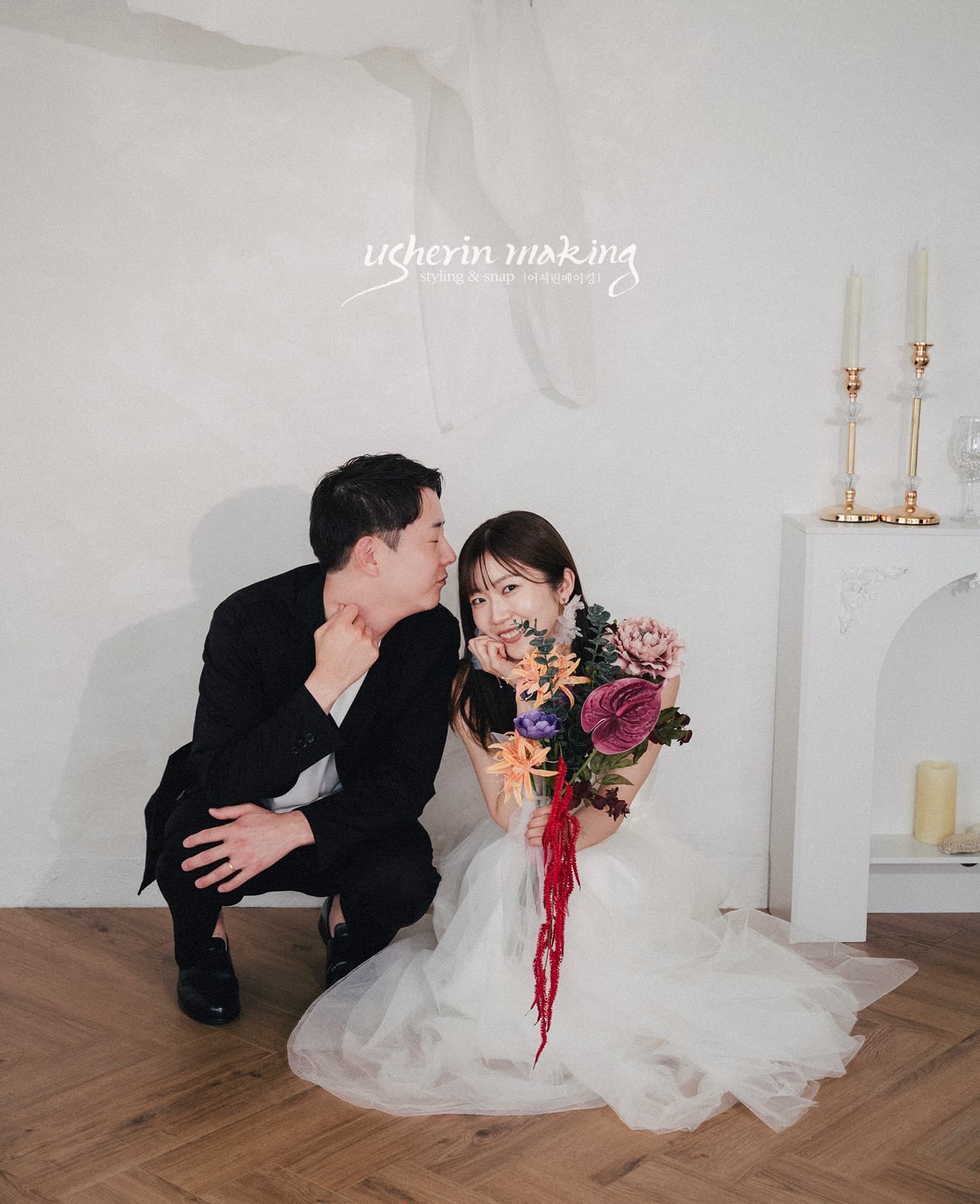 Couple sitting close on a white studio floor, the bride holding a purple bouquet