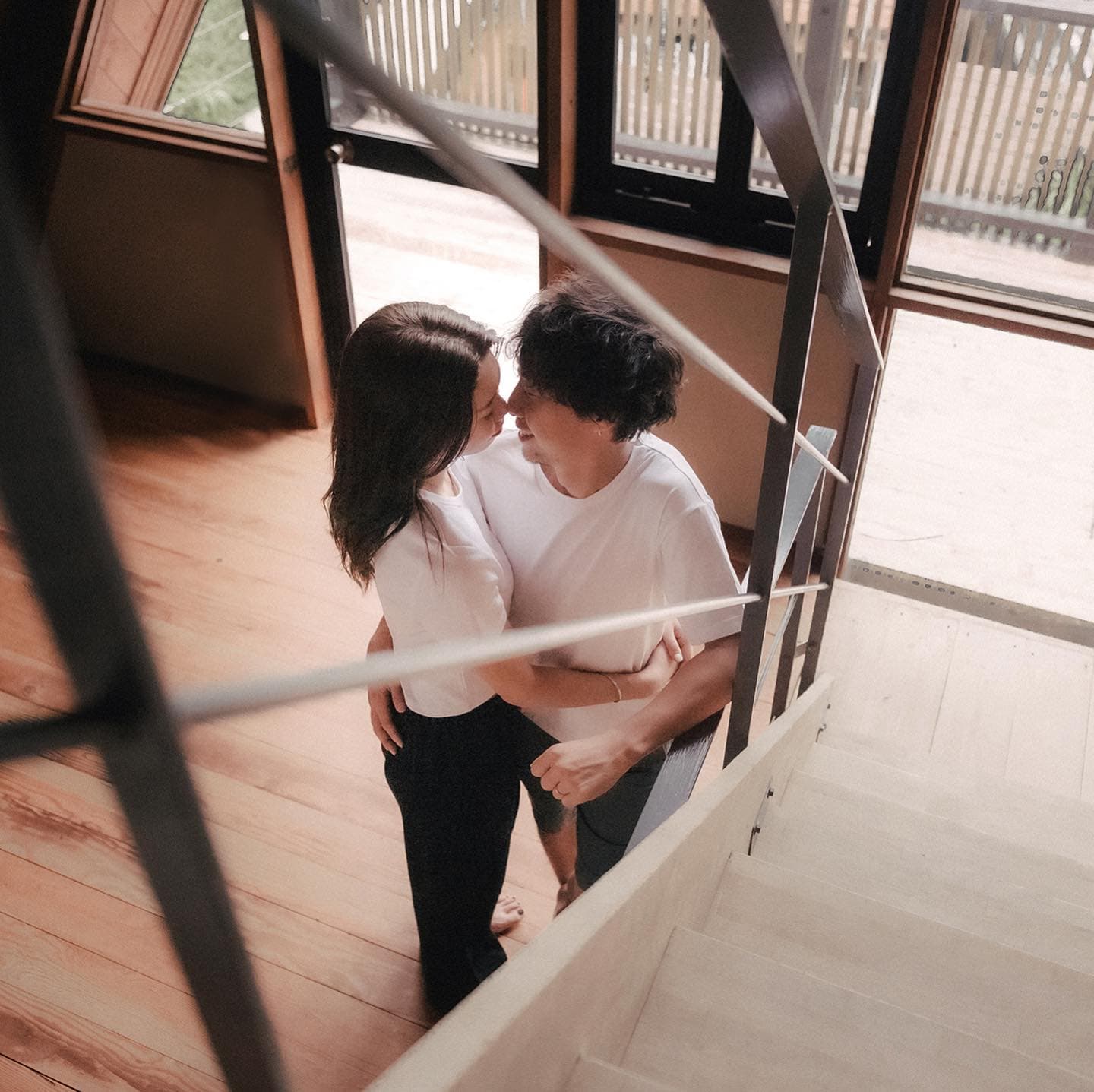 Couple embracing at the foot of the stairs in a warm wooden interior