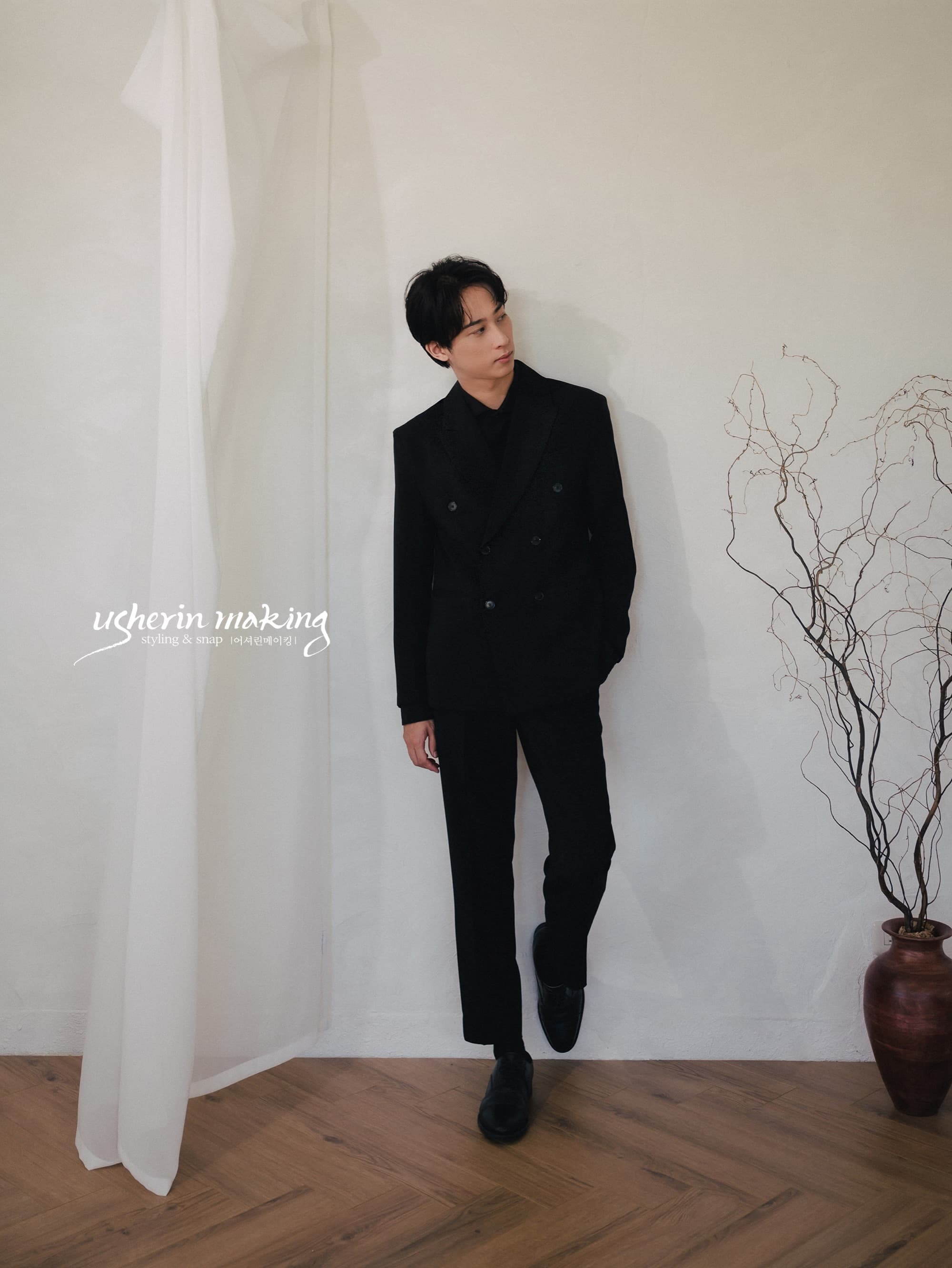 Groom in a black double-breasted suit standing alone in a white studio