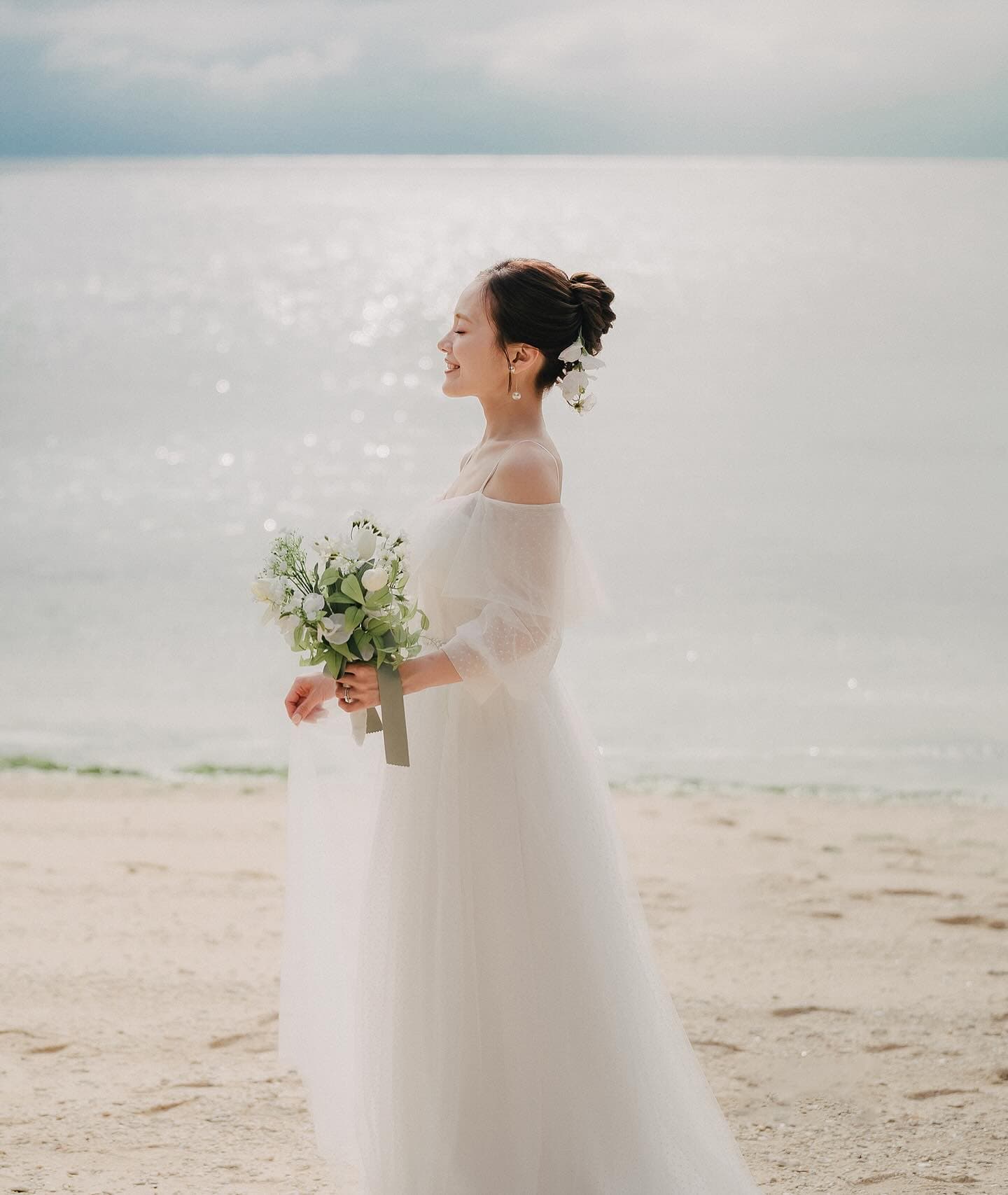 Bride in a white gown holding a bouquet by the shimmering Okinawa sea