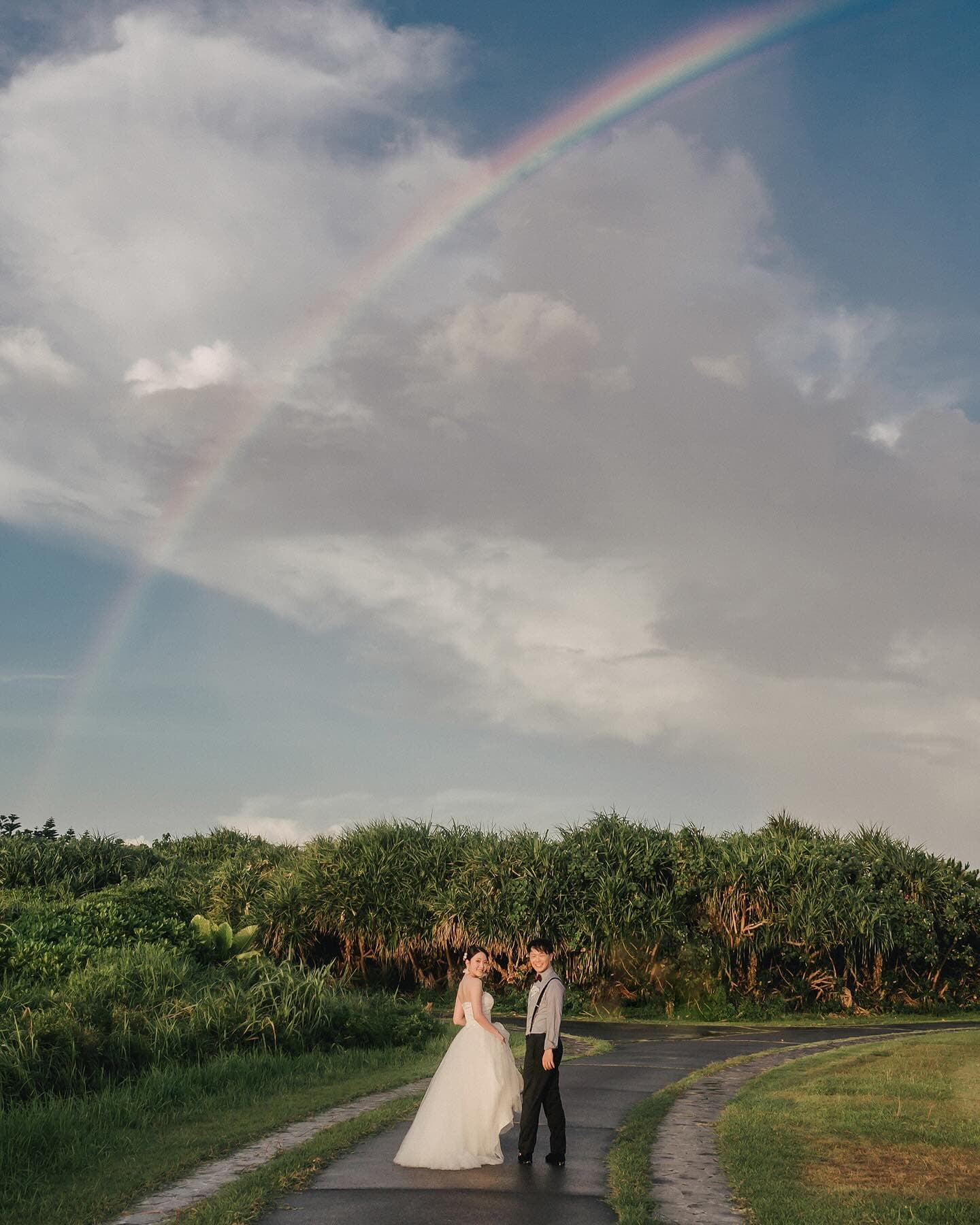 Bride and groom on a green lane under a rainbow after rain in Okinawa