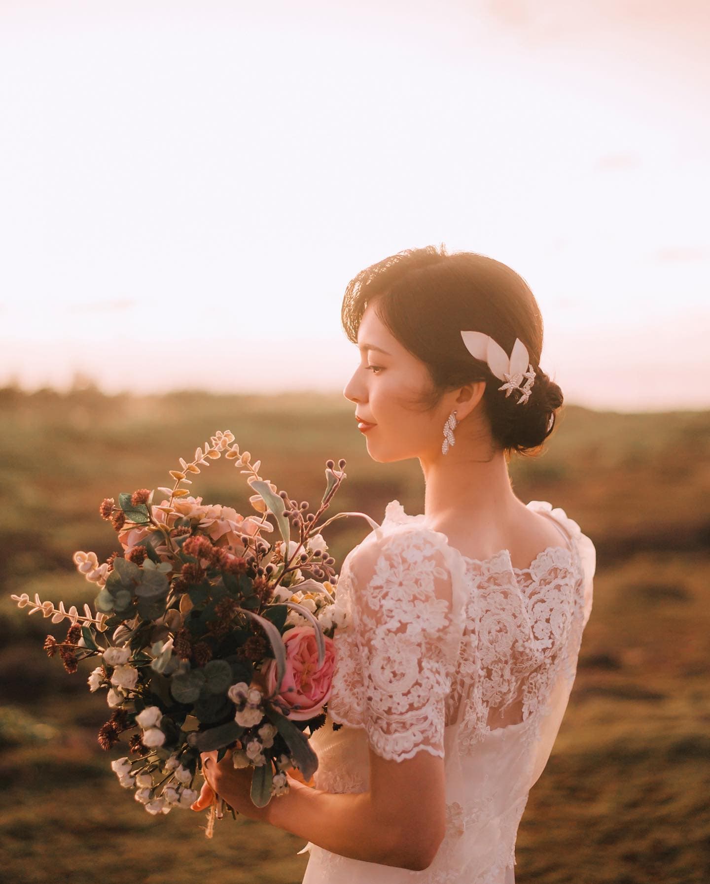 Bride in a lace-back dress holding a full bouquet in warm golden evening light