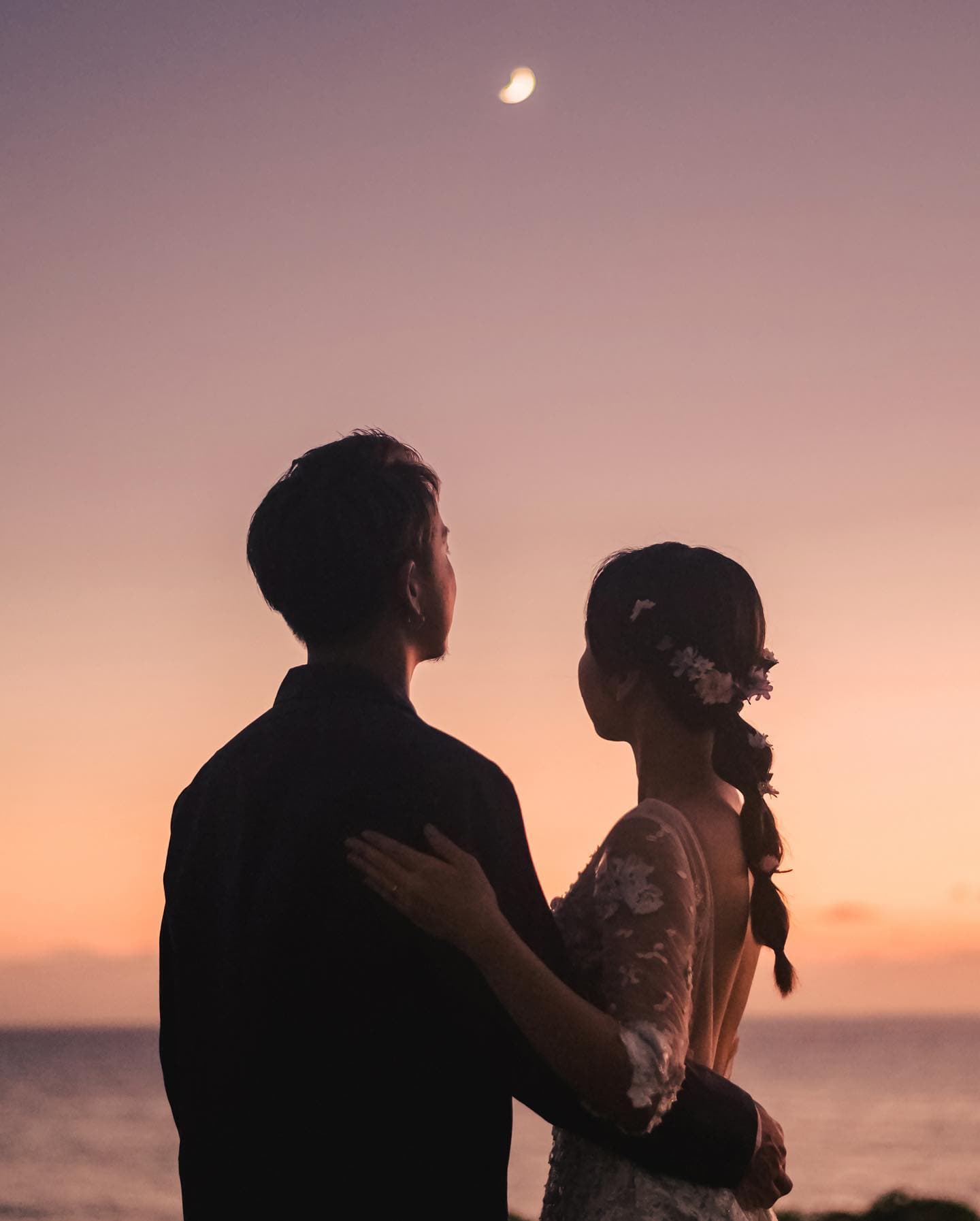 夕焼けの空に浮かぶ三日月を見上げる新郎新婦