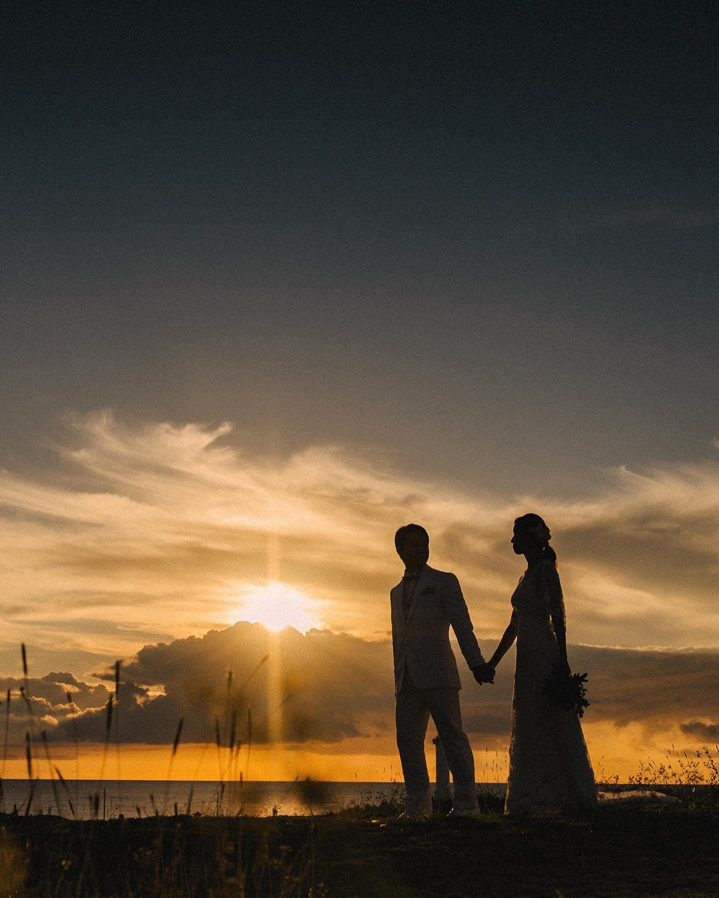 Silhouetted couple hold hands before a blazing sunset over the Okinawa sea