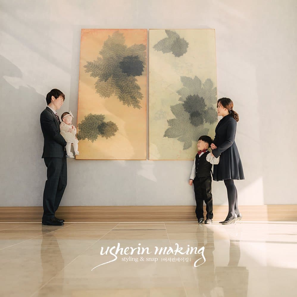 커다란 그림 앞에 마주 선 정장 차림의 가족