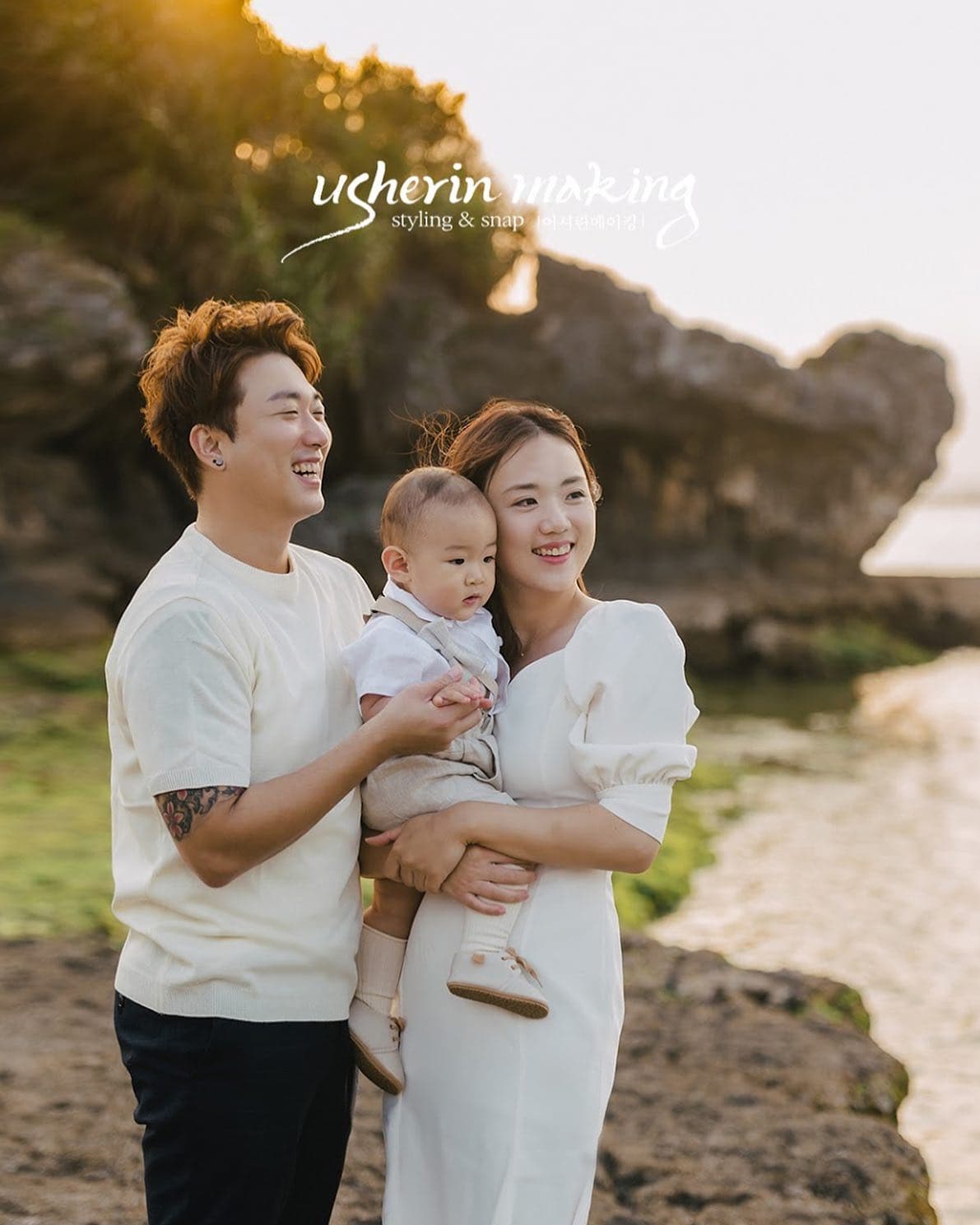 노을빛 오키나와 바위 해안에서 아기를 안고 웃는 흰 옷차림의 가족