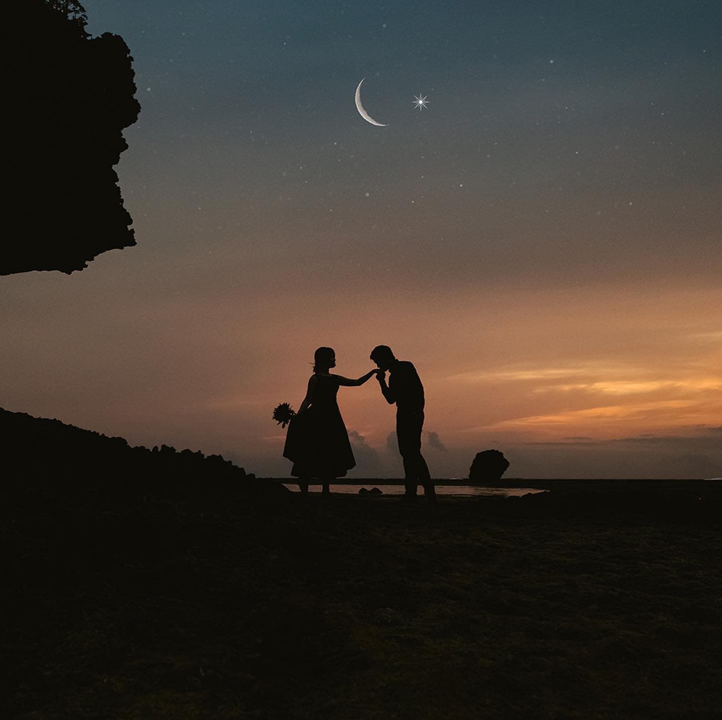 三日月の浮かぶ夕暮れの空の下、手にキスするカップルのシルエット、沖縄