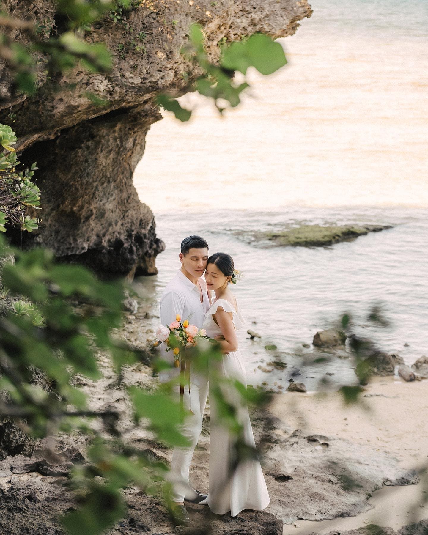 Couple embracing in a rocky cove by the pale Okinawa sea