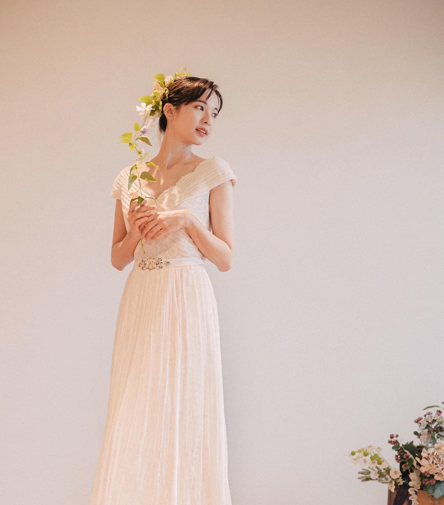 Bride with greenery in her hair holding a flowering branch against a plain wall