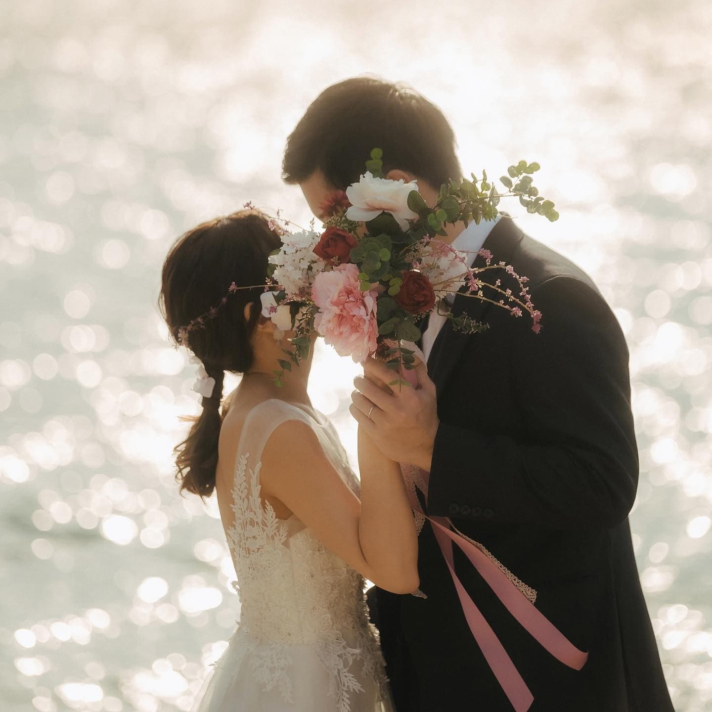 Couple stealing a kiss behind their bouquet against a glittering Okinawa sea