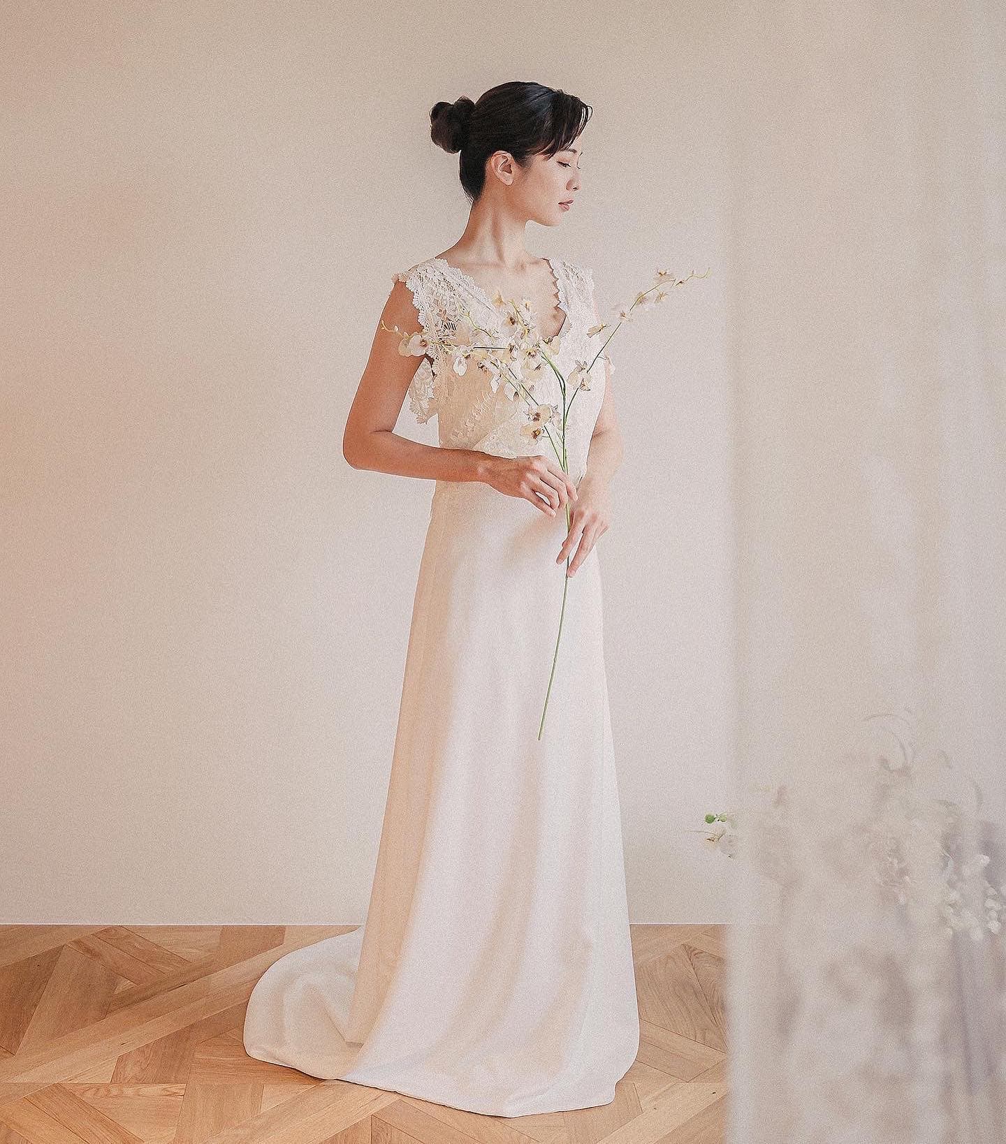 Bride in a long ivory dress holding a tall orchid branch in a simple studio