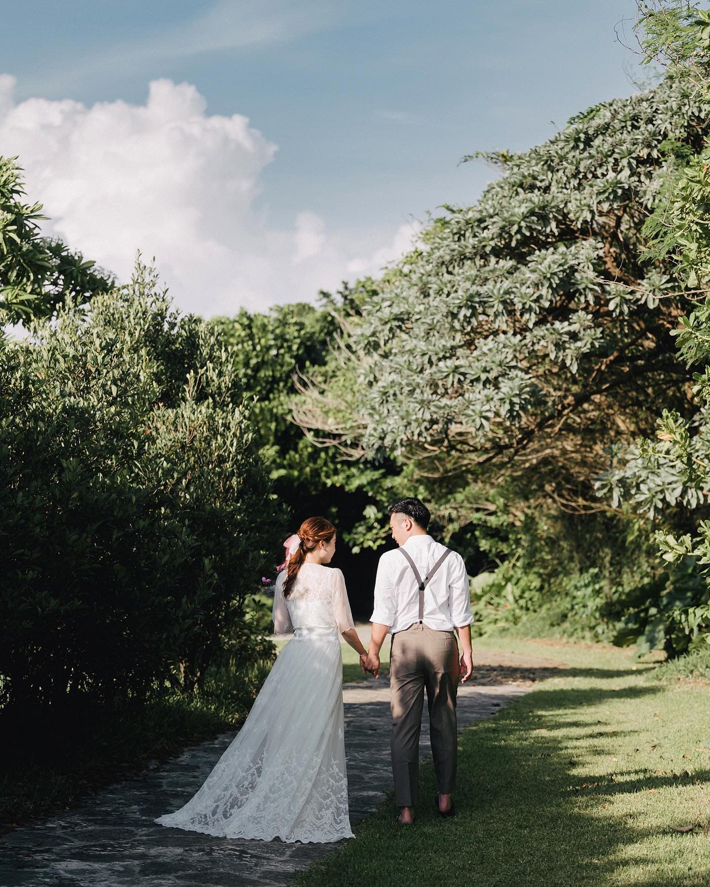 Bride and groom walking hand in hand along a leafy Okinawa stone path