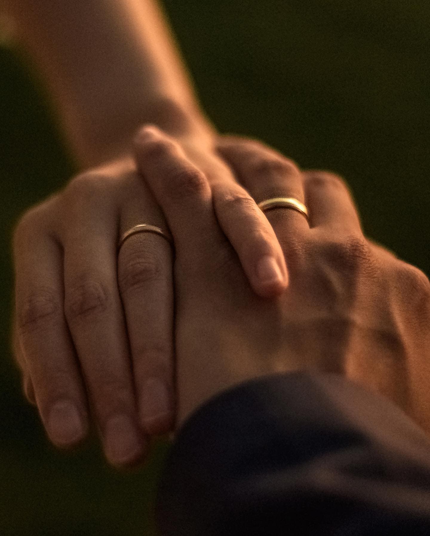 夕暮れの光の中、結婚指輪を着けた手を重ねるふたり
