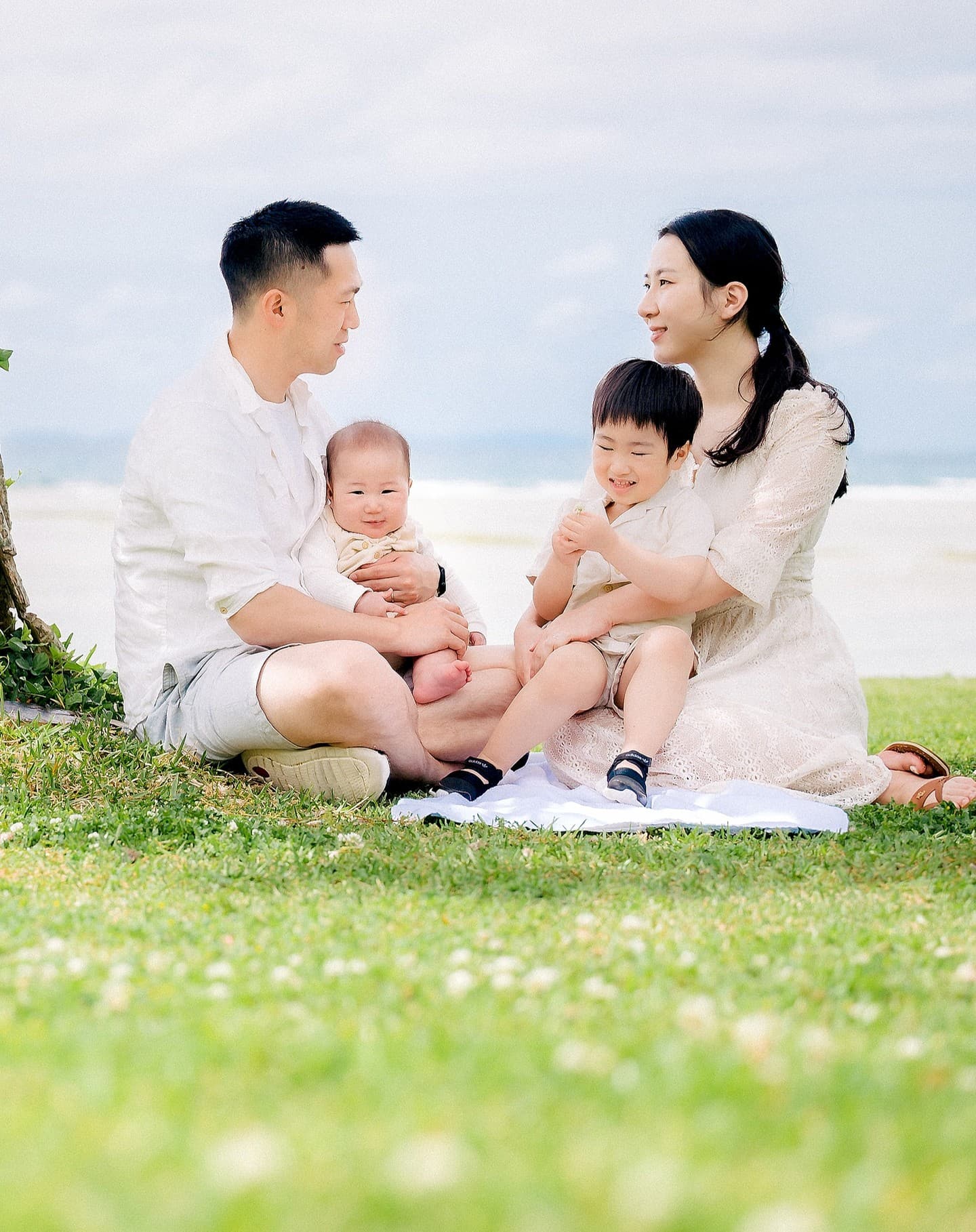 잔디밭에 둘러앉아 웃음 짓는 네 식구와 오키나와 바다