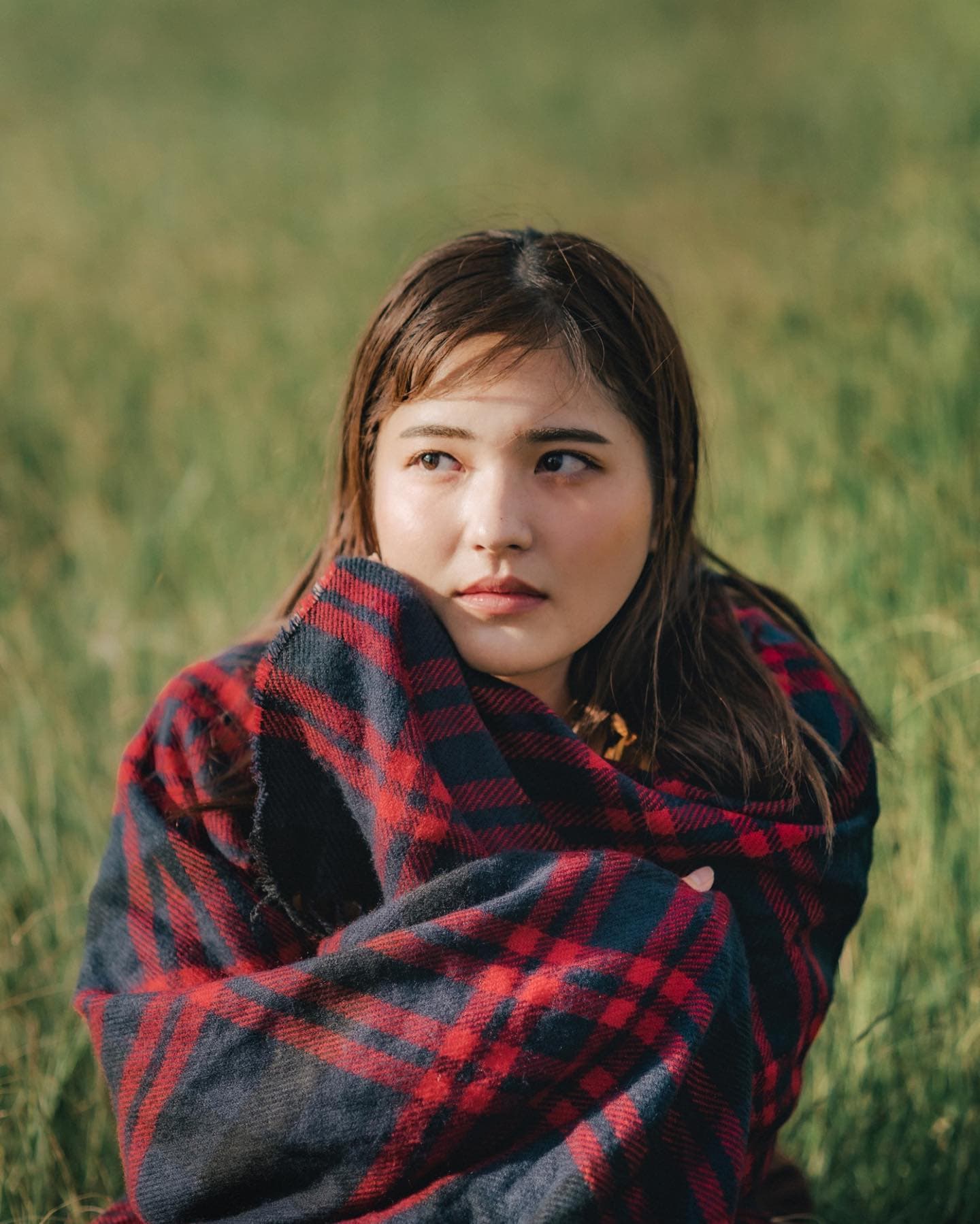 Portrait of a woman wrapped in a plaid blanket in a grassy field in Okinawa