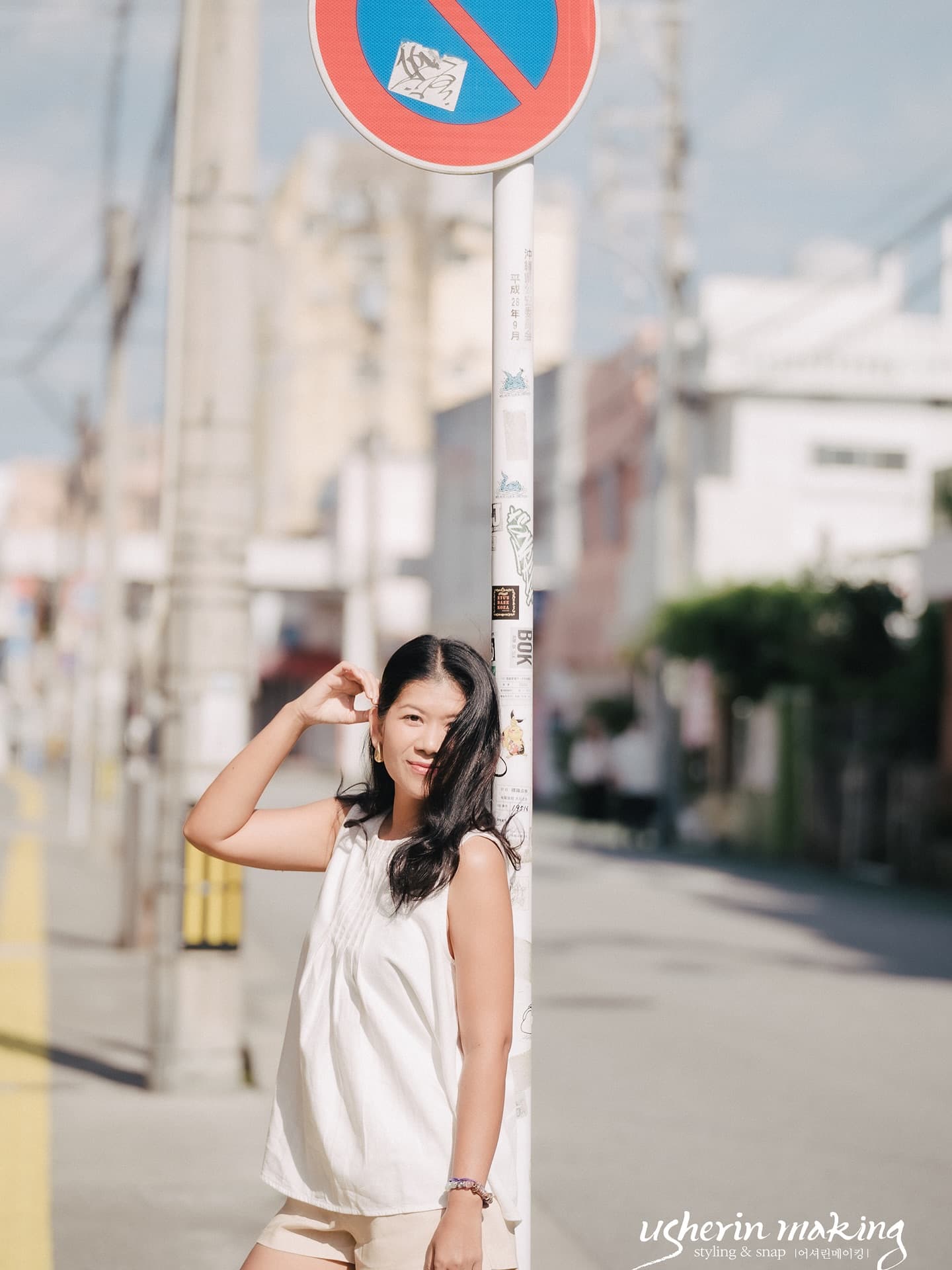 Woman in a white top posing by a street sign pole on a retro Okinawa street