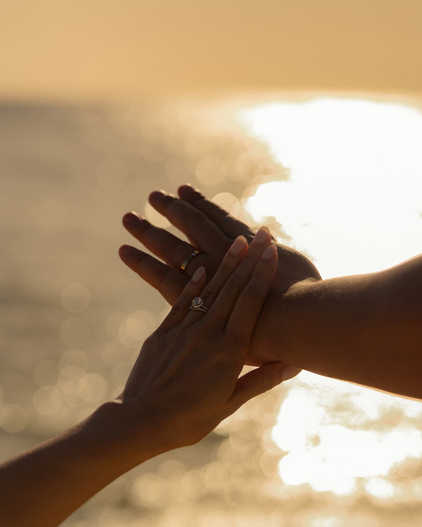夕日にきらめく海を背に結婚指輪の手を重ねるクローズアップ、沖縄