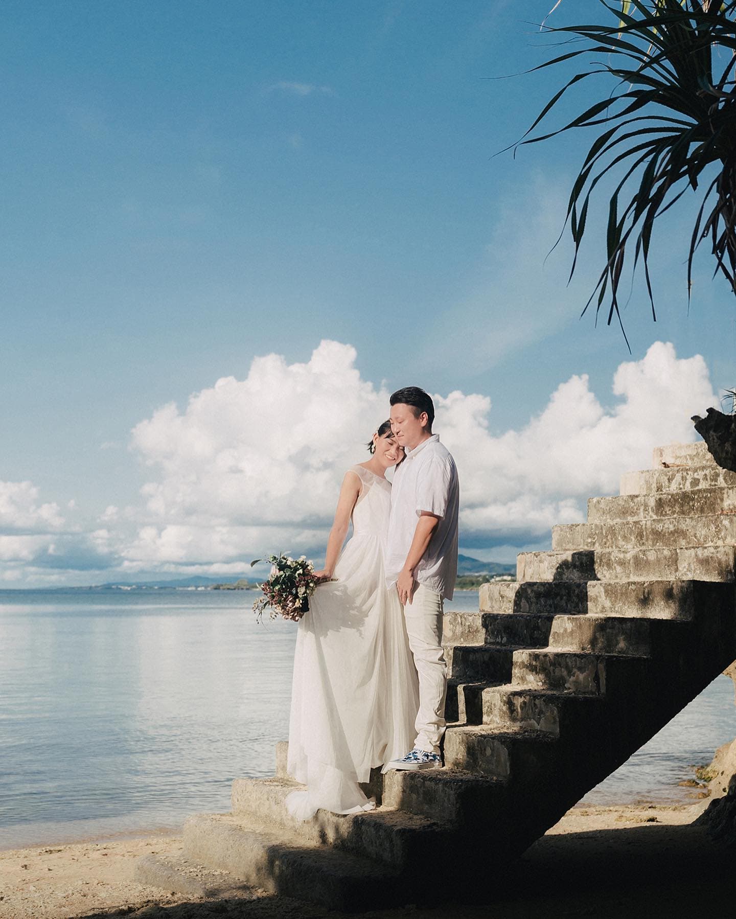 Couple nestled on old stone steps by the sea under a clear blue Okinawa sky