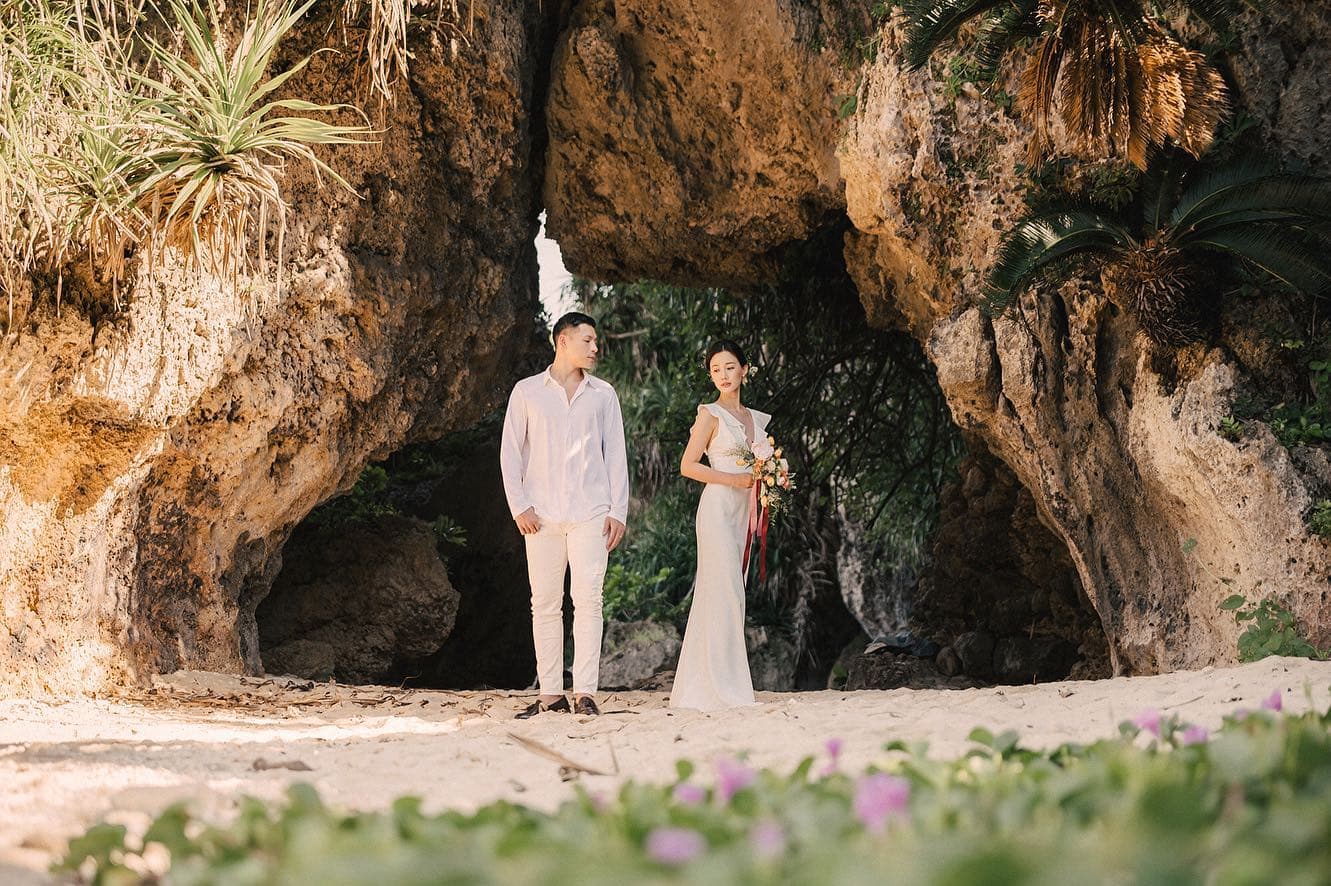 Bride and groom stand beneath a natural rock arch on an Okinawa beach