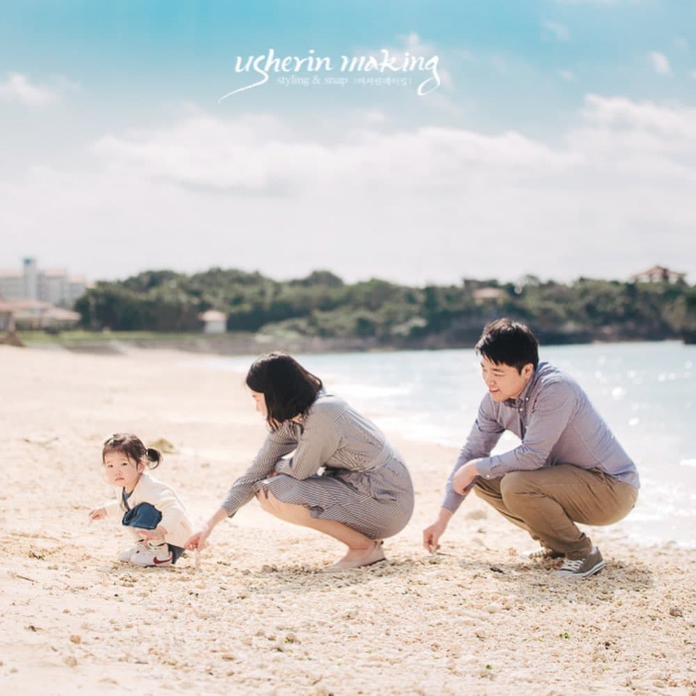 Parents crouch beside their little girl playing in the sand on a sunny Okinawa beach