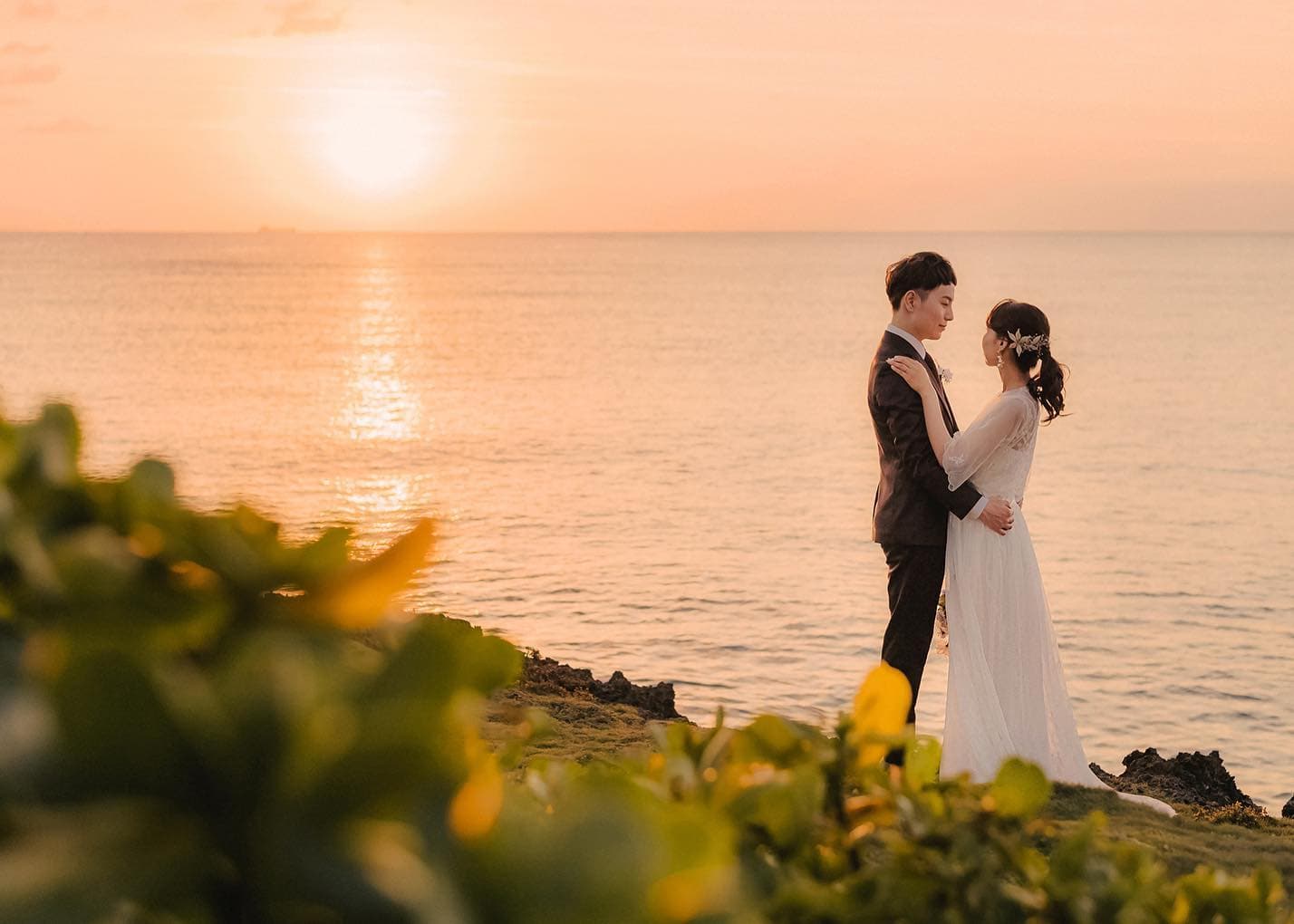 海に沈む夕日を背に崖の上で抱き合う新郎新婦