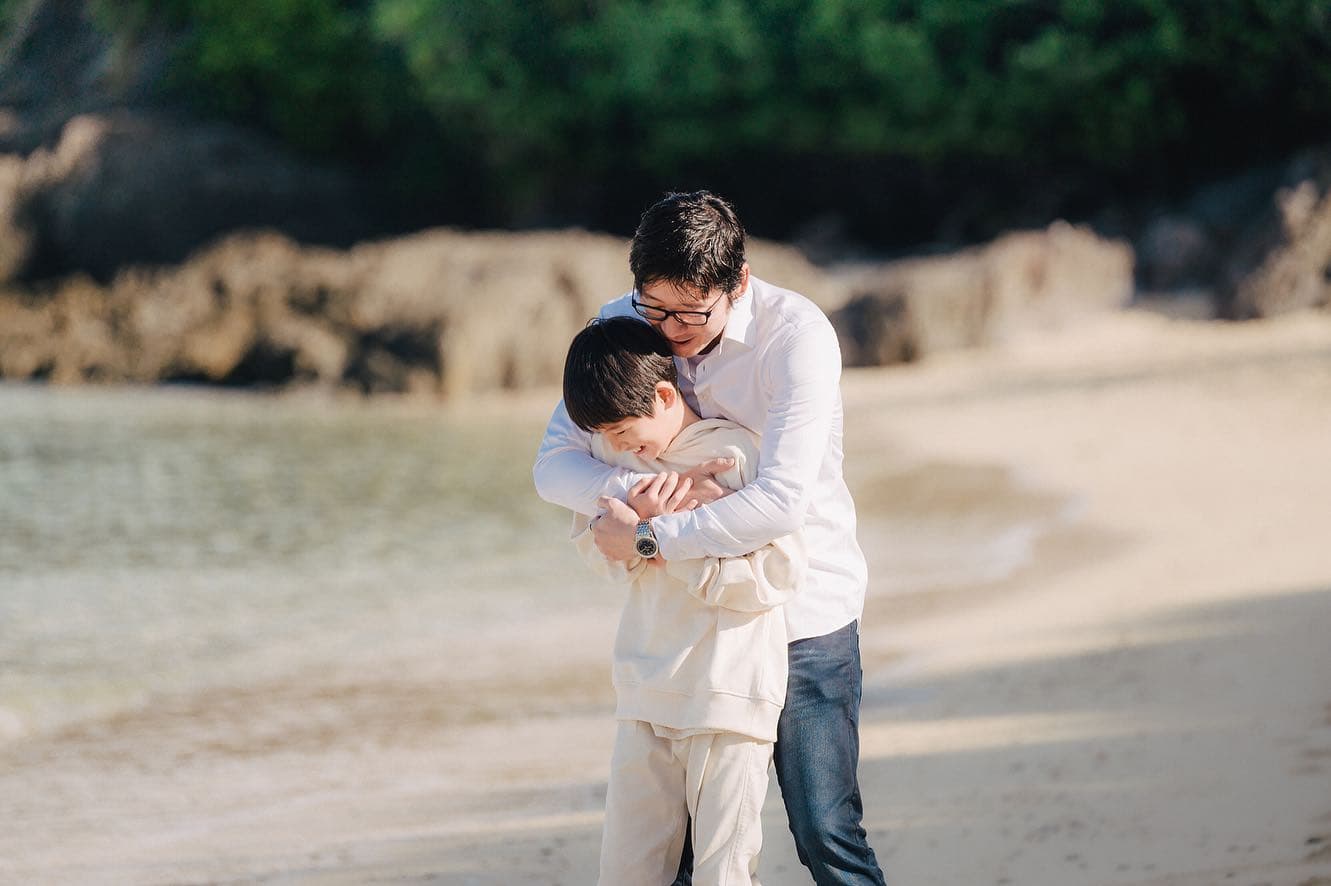沖縄の浜辺で息子を後ろから抱きしめる父親