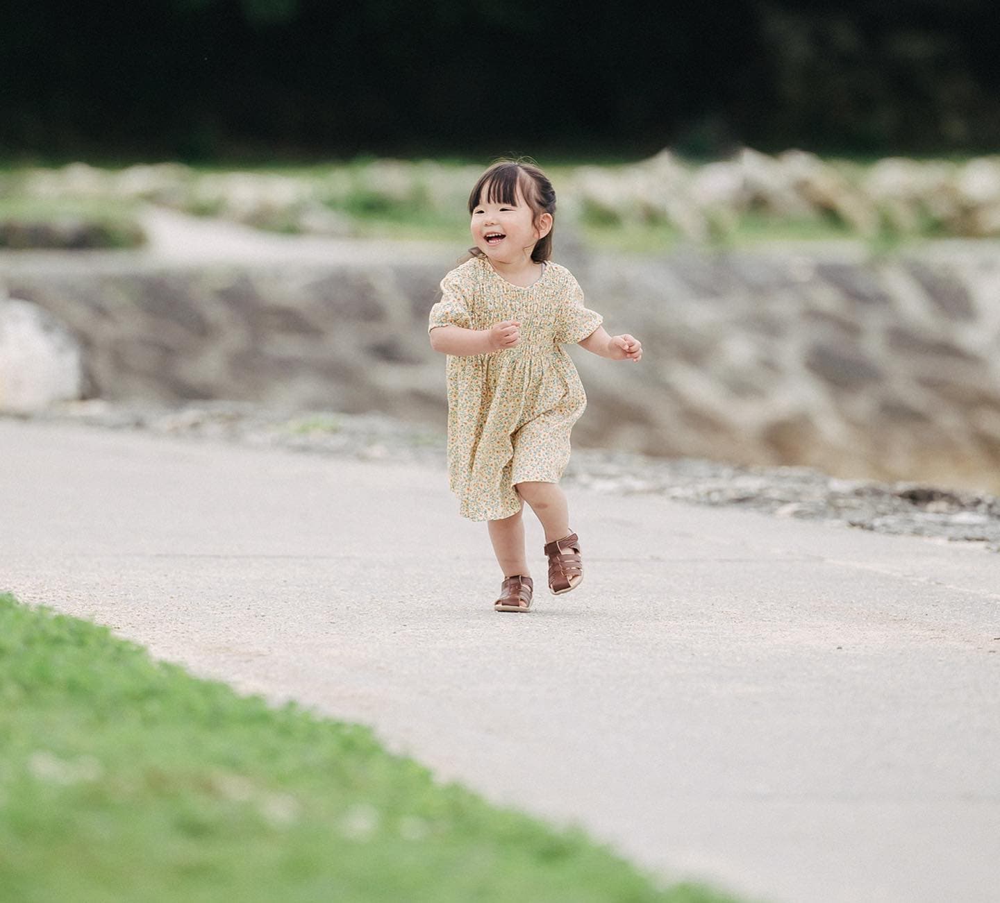 石畳の小道を笑顔で駆けてくる花柄ワンピースの女の子