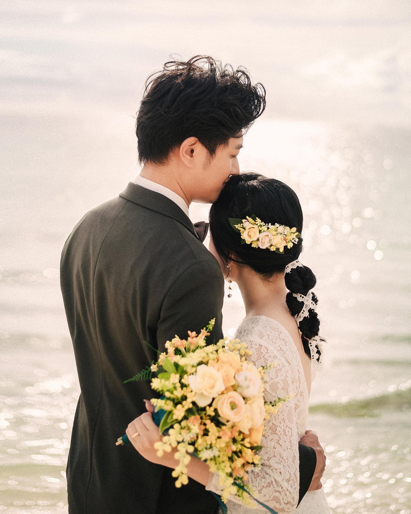 반짝이는 바다를 앞에 두고 신부의 머리에 입 맞추는 신랑의 뒷모습
