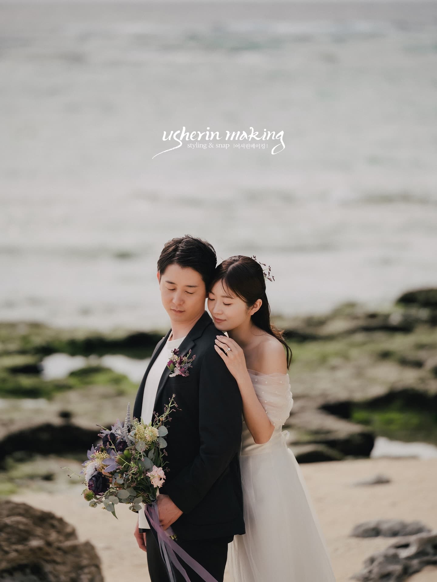 A bride rests on her groom's shoulder on a rocky Okinawa shore