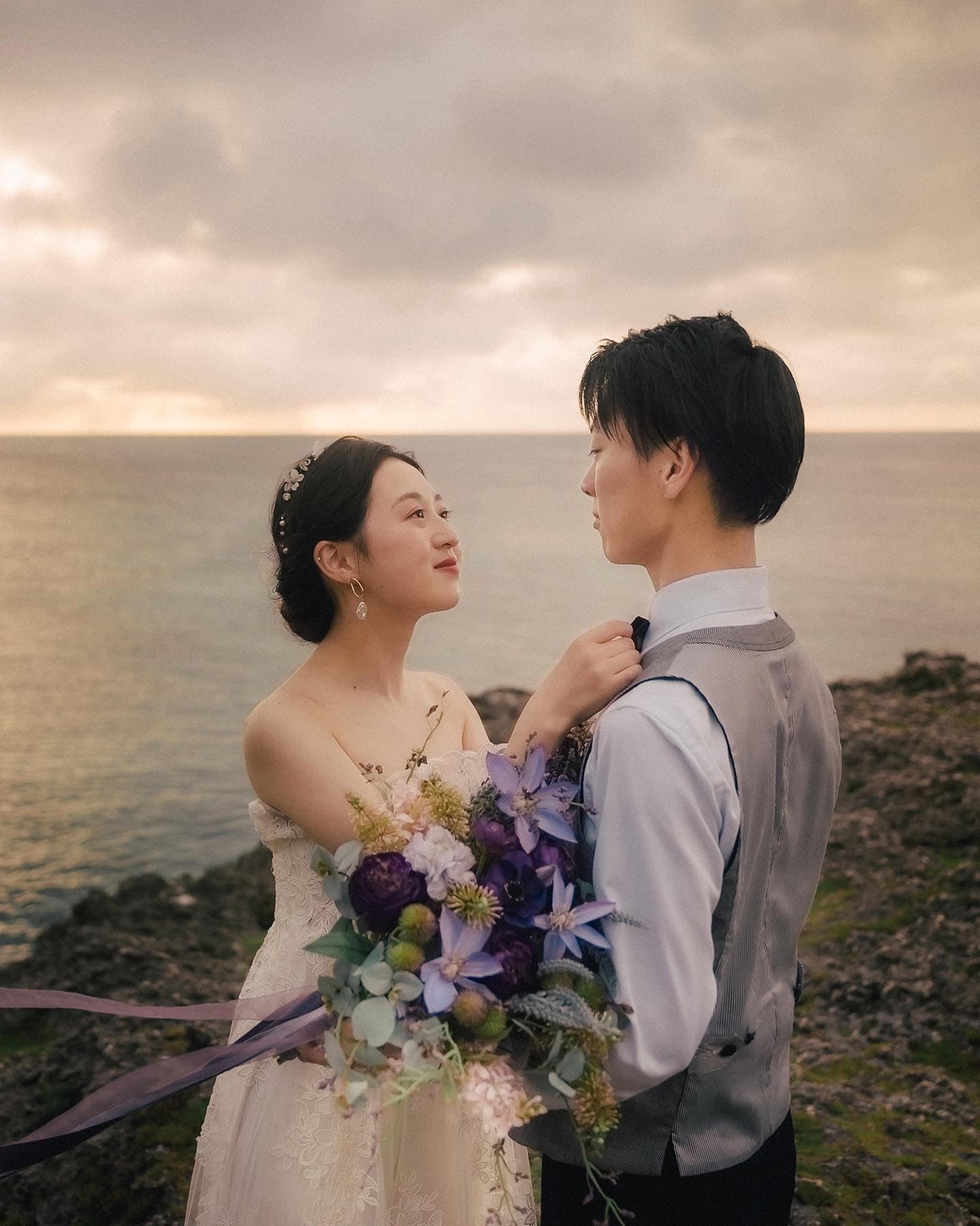 Bride with a purple bouquet gazing at the groom on an overcast Okinawa coast