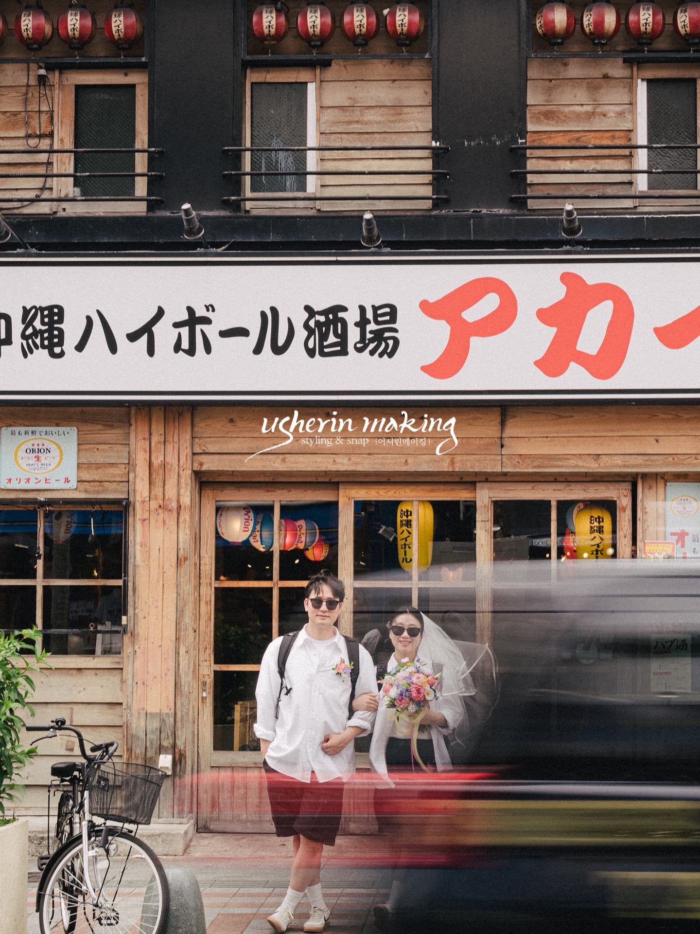 Casually dressed couple with veil and bouquet outside an Okinawan izakaya with red lanterns