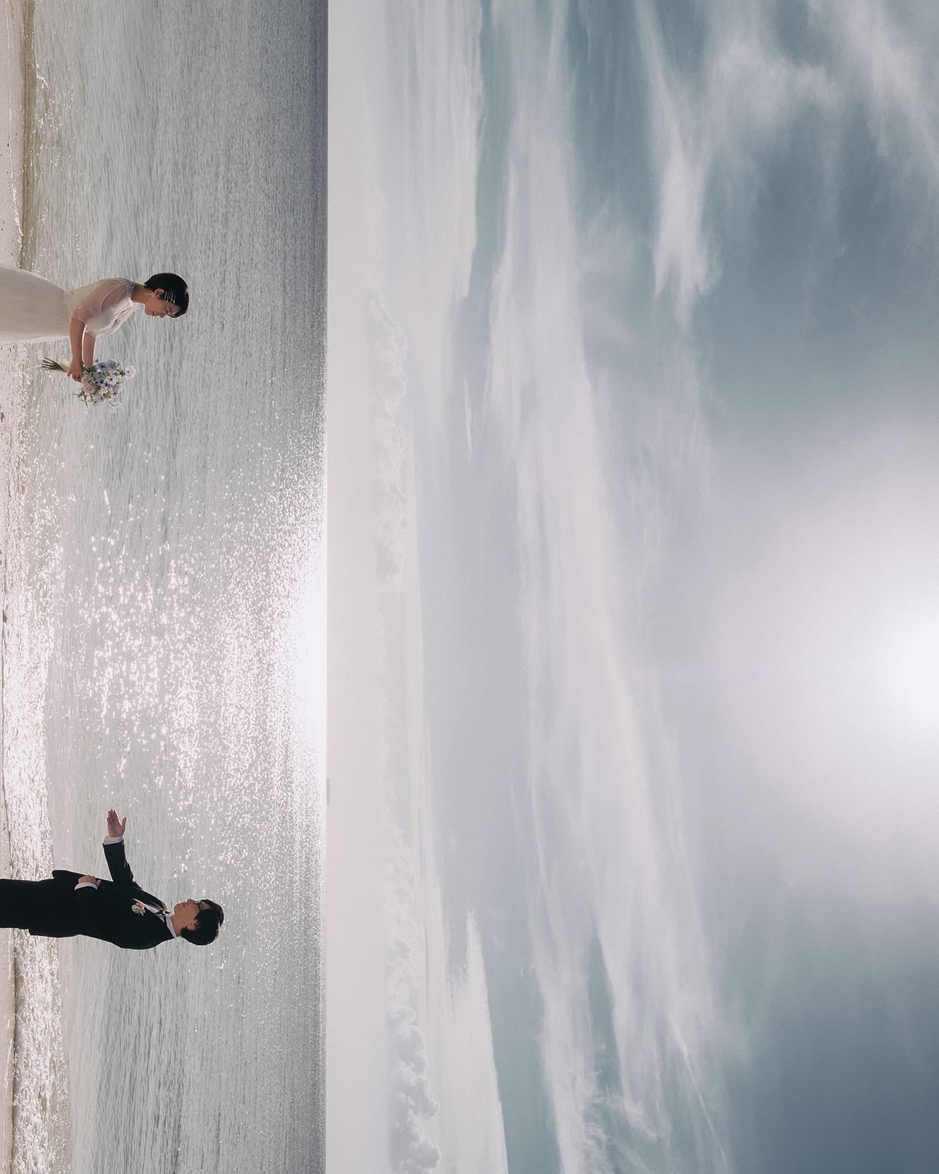 Bride and groom playfully apart on a sparkling shoreline in Okinawa