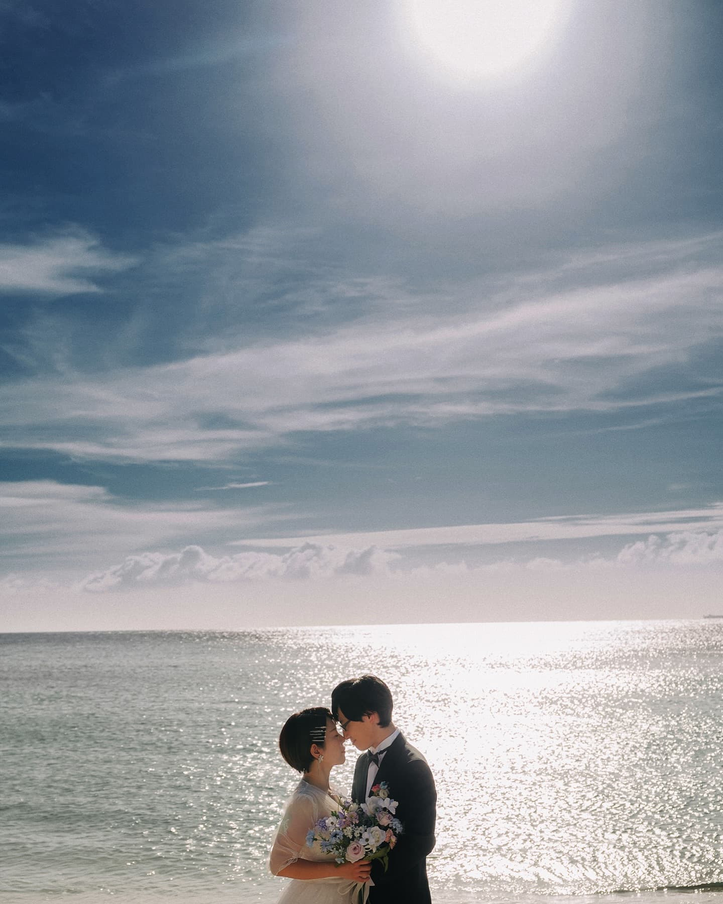 Couple embracing by the glittering sea under bright sun in Okinawa
